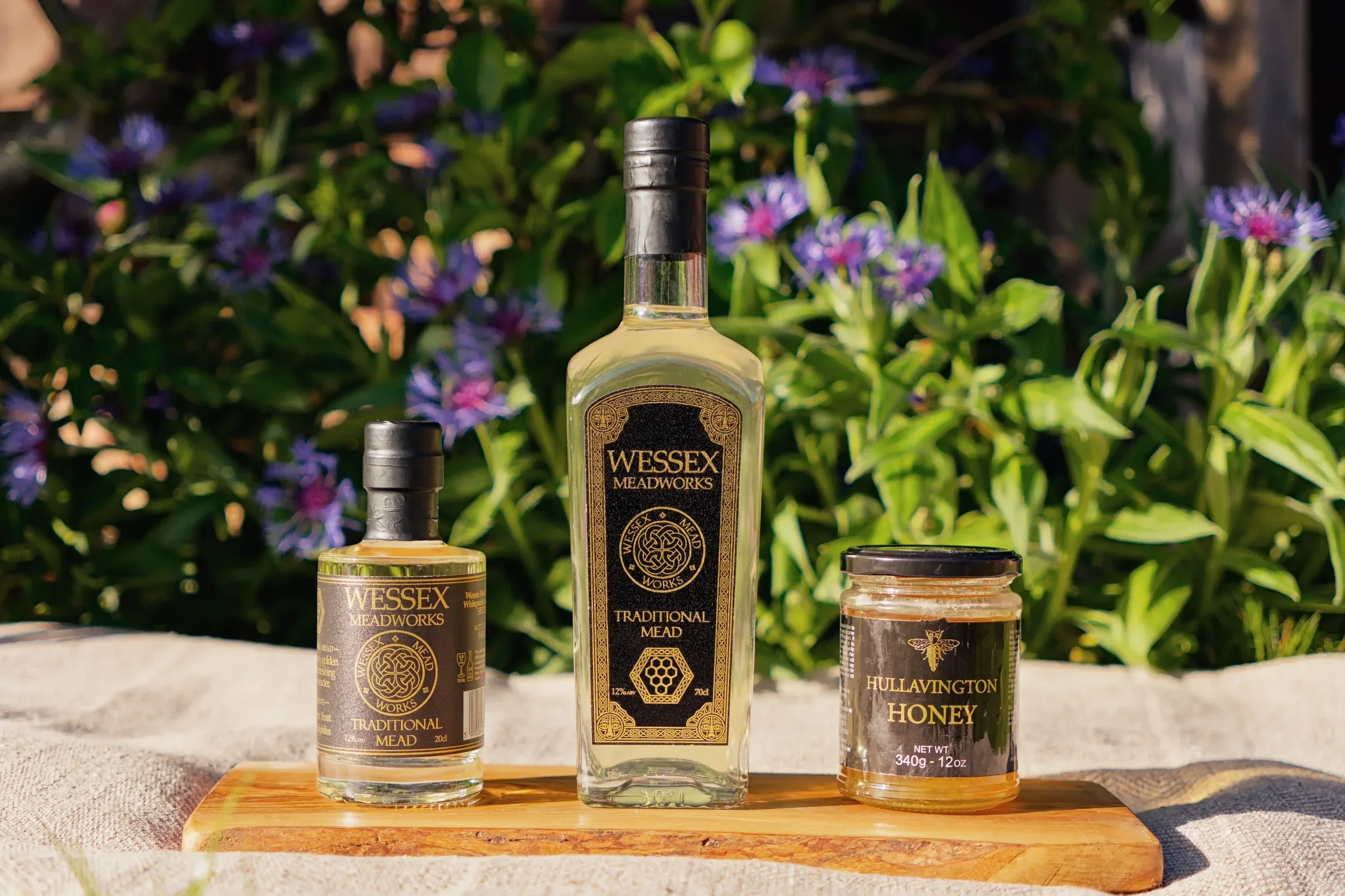 Wessex Meadworks bottles of mead, jar of honey, on wood tray, flowers.
