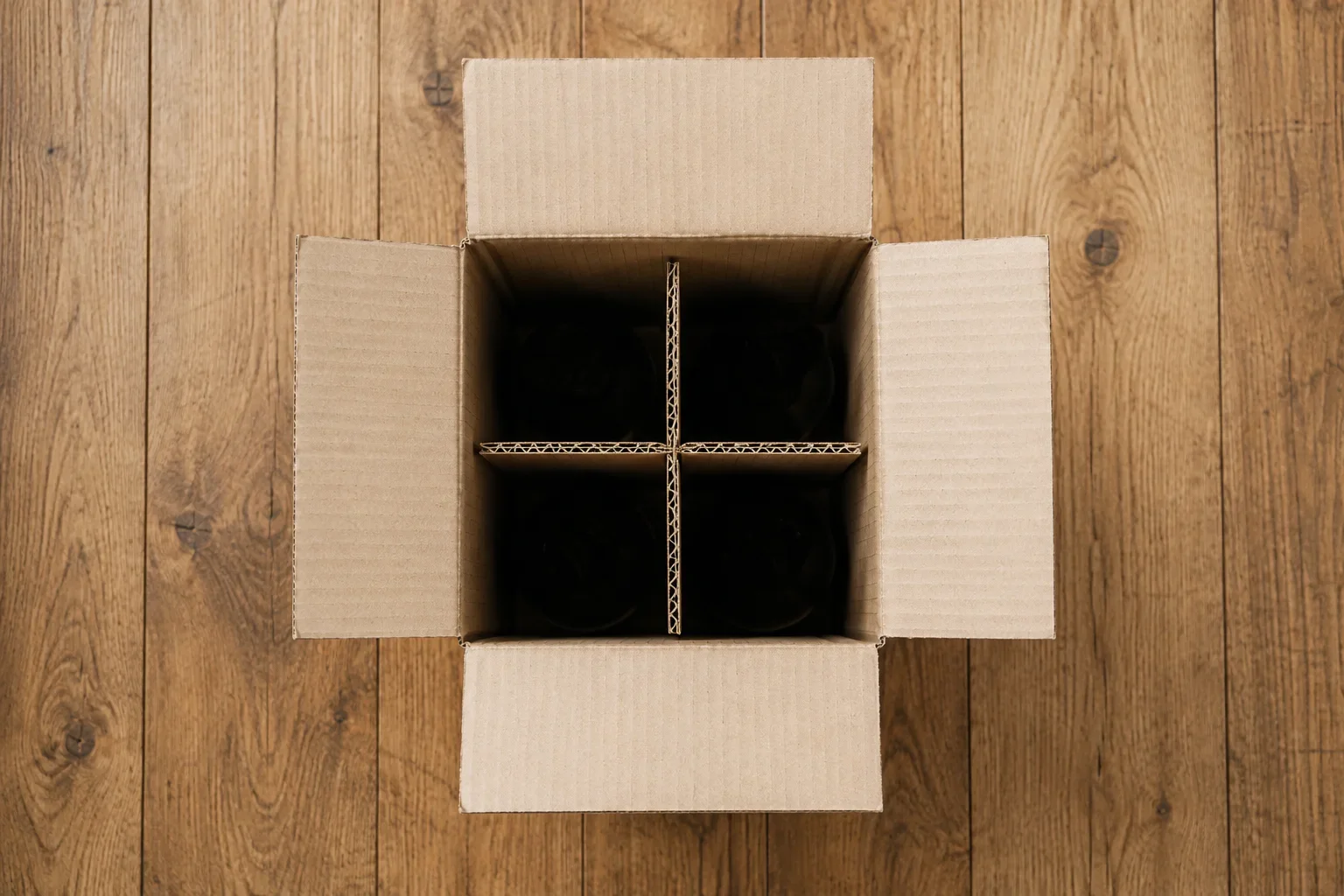 Open cardboard shipping box with grid for bottles, top down.