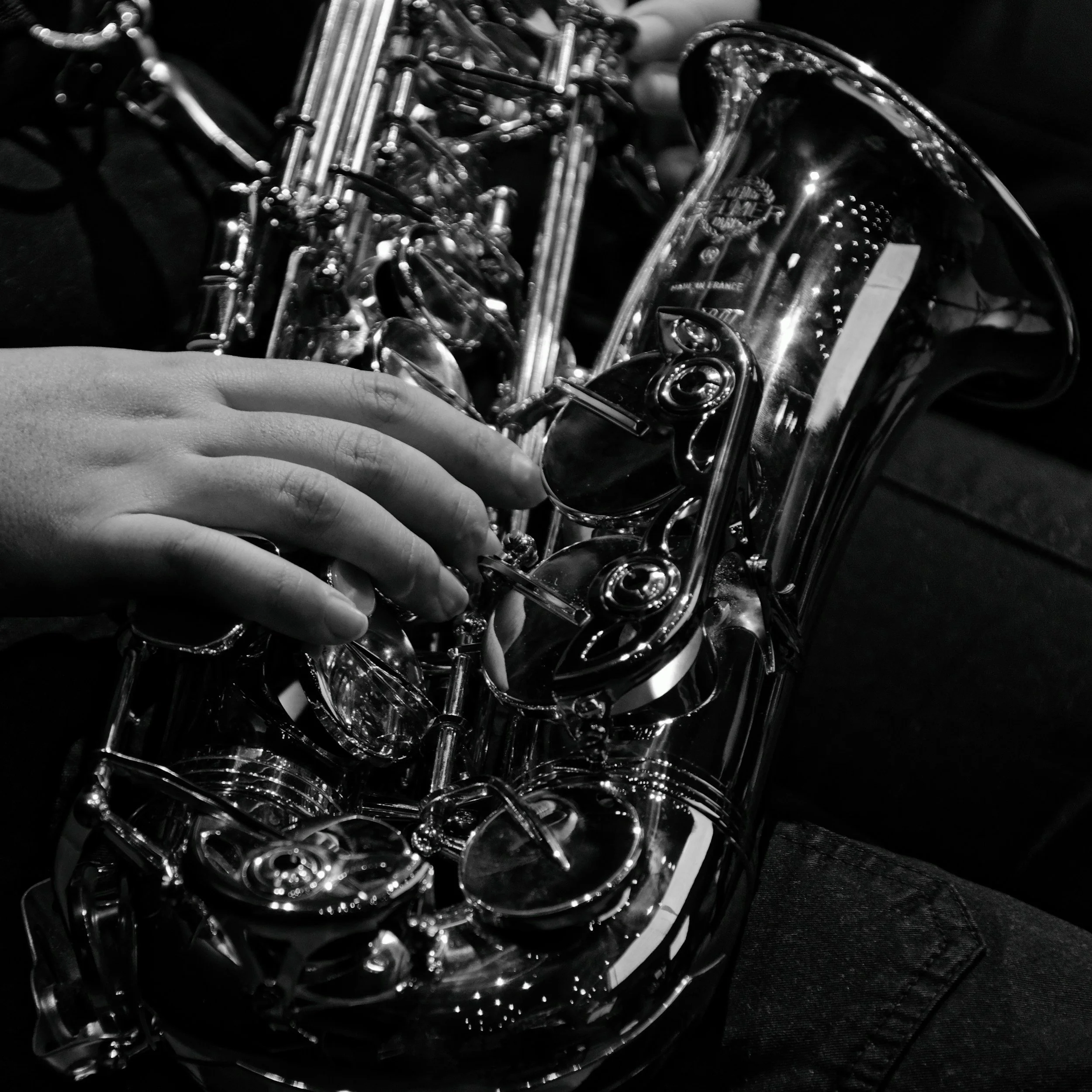 A hand playing a silver saxophone, with intricate details and reflections on the instrument, in black and white.