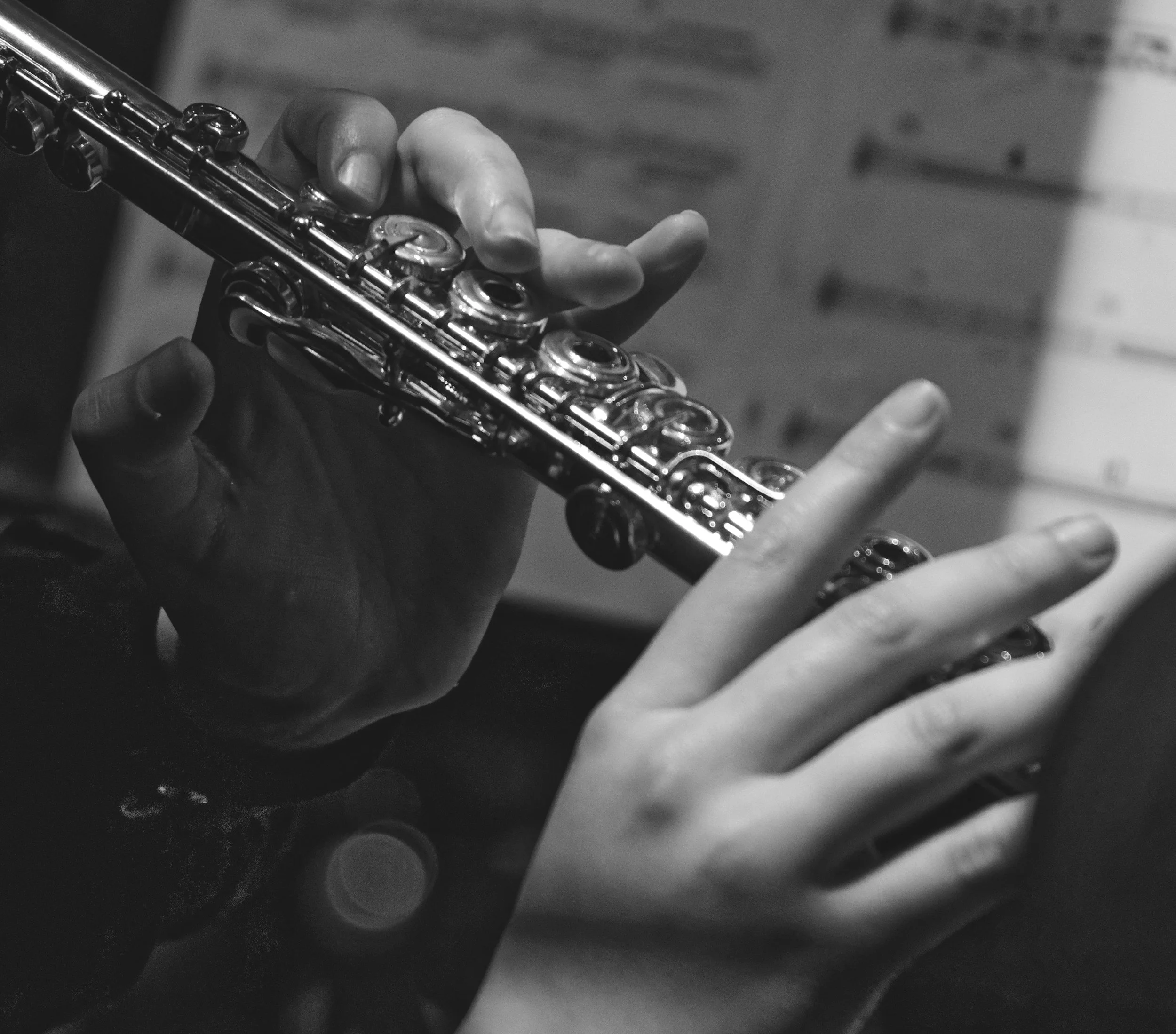 A close-up black and white photo of two hands playing a flute, with a wooden background.