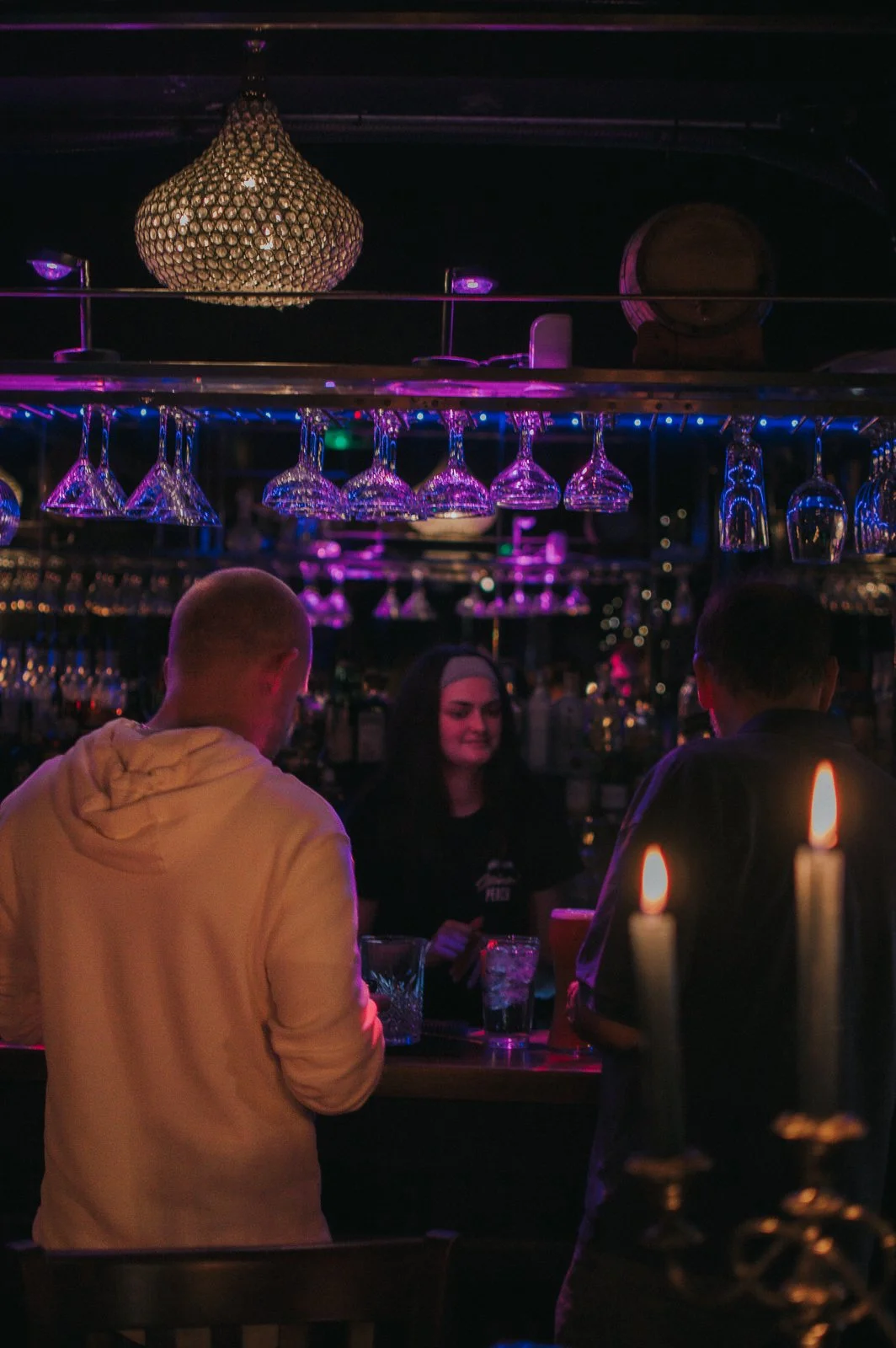 People at a bar talking, with hanging glasses and a crystal chandelier overhead