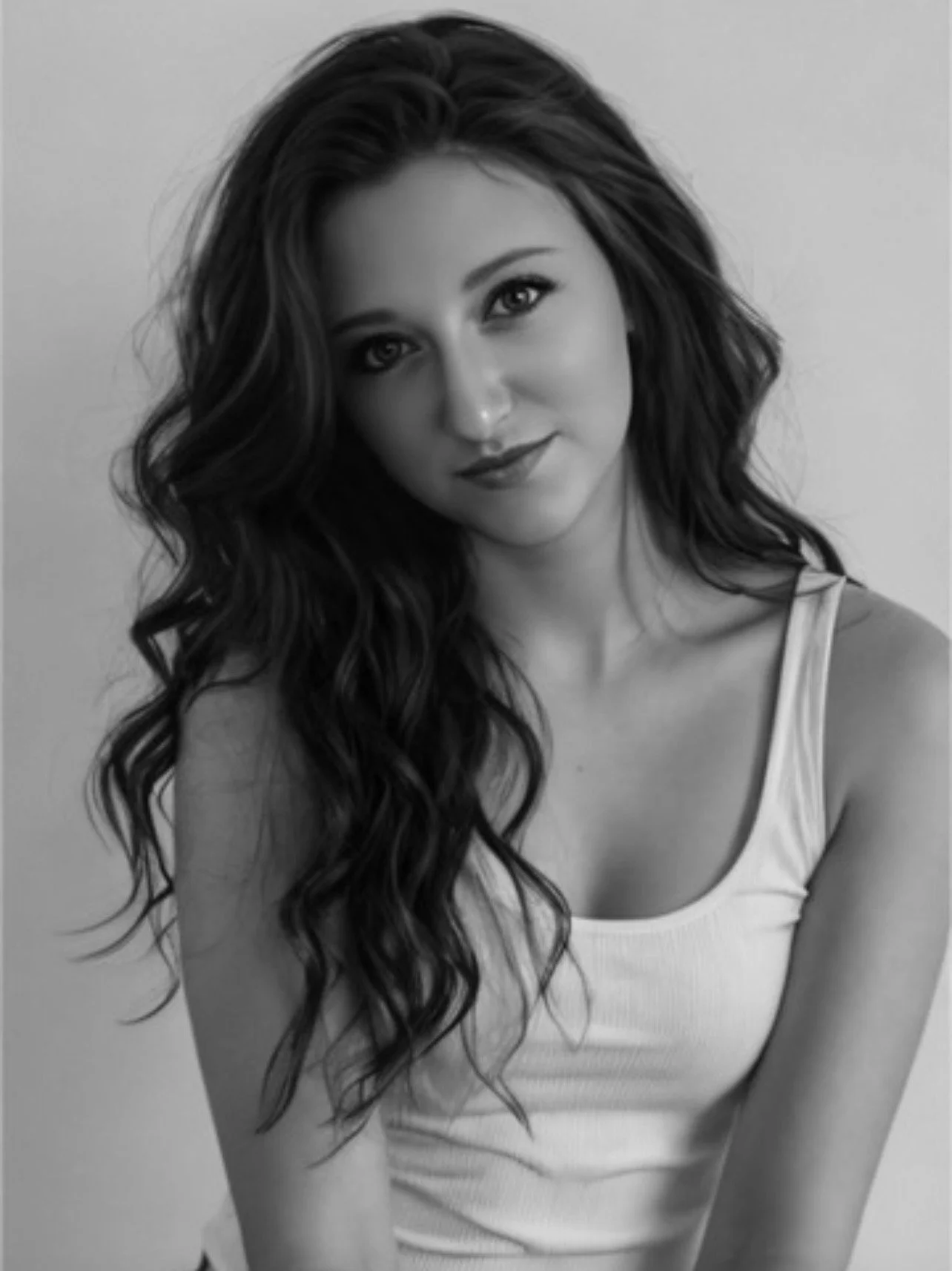 Black and white photograph of a young woman with long, wavy hair, wearing a sleeveless top, looking at the camera with a slight smile.