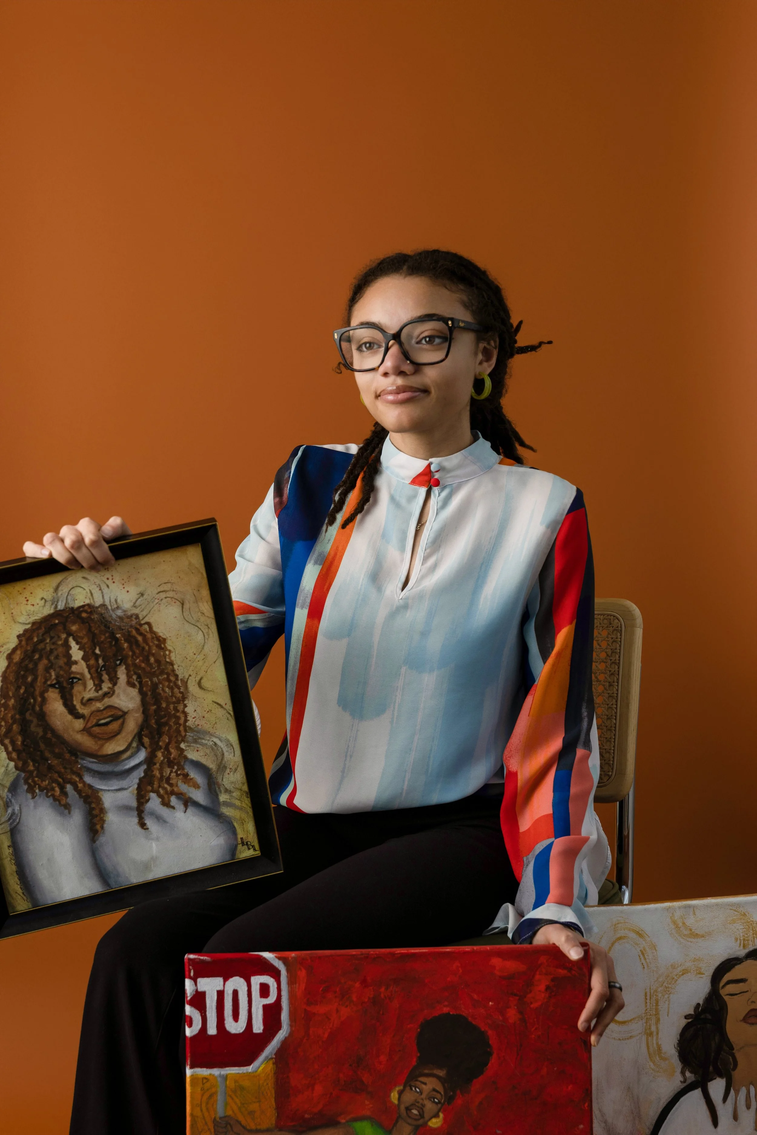 London B (LBL) with loc's, wearing glasses  sits against an orange background, holding original LBL painting.