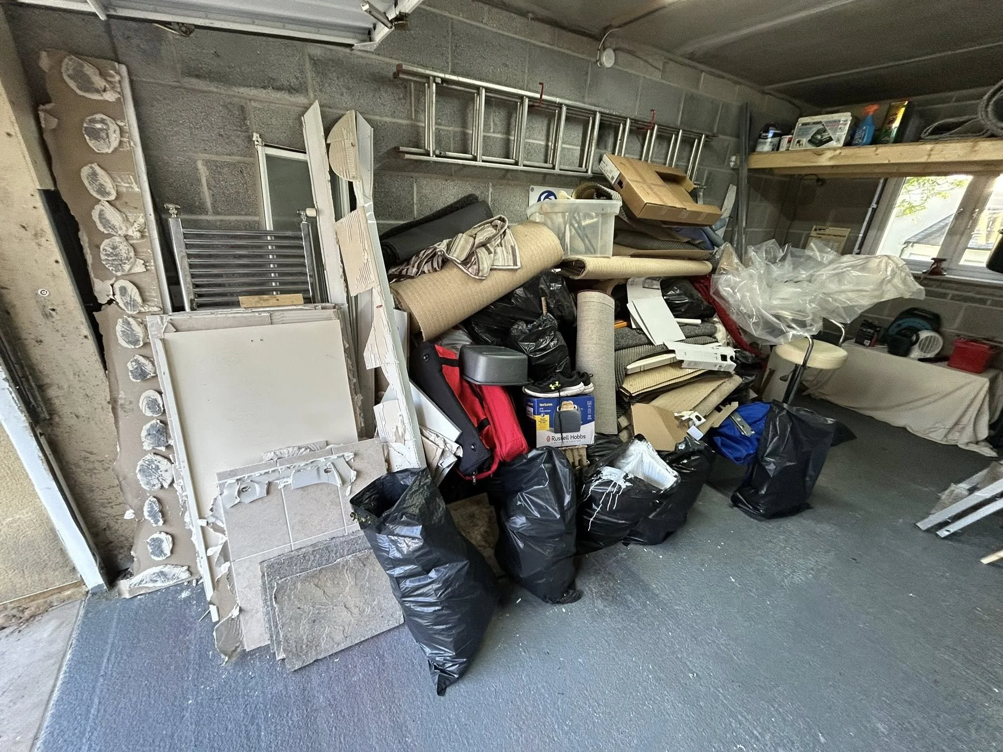 Messy garage or workshop with various construction debris, tools, bags, and miscellaneous items scattered around.