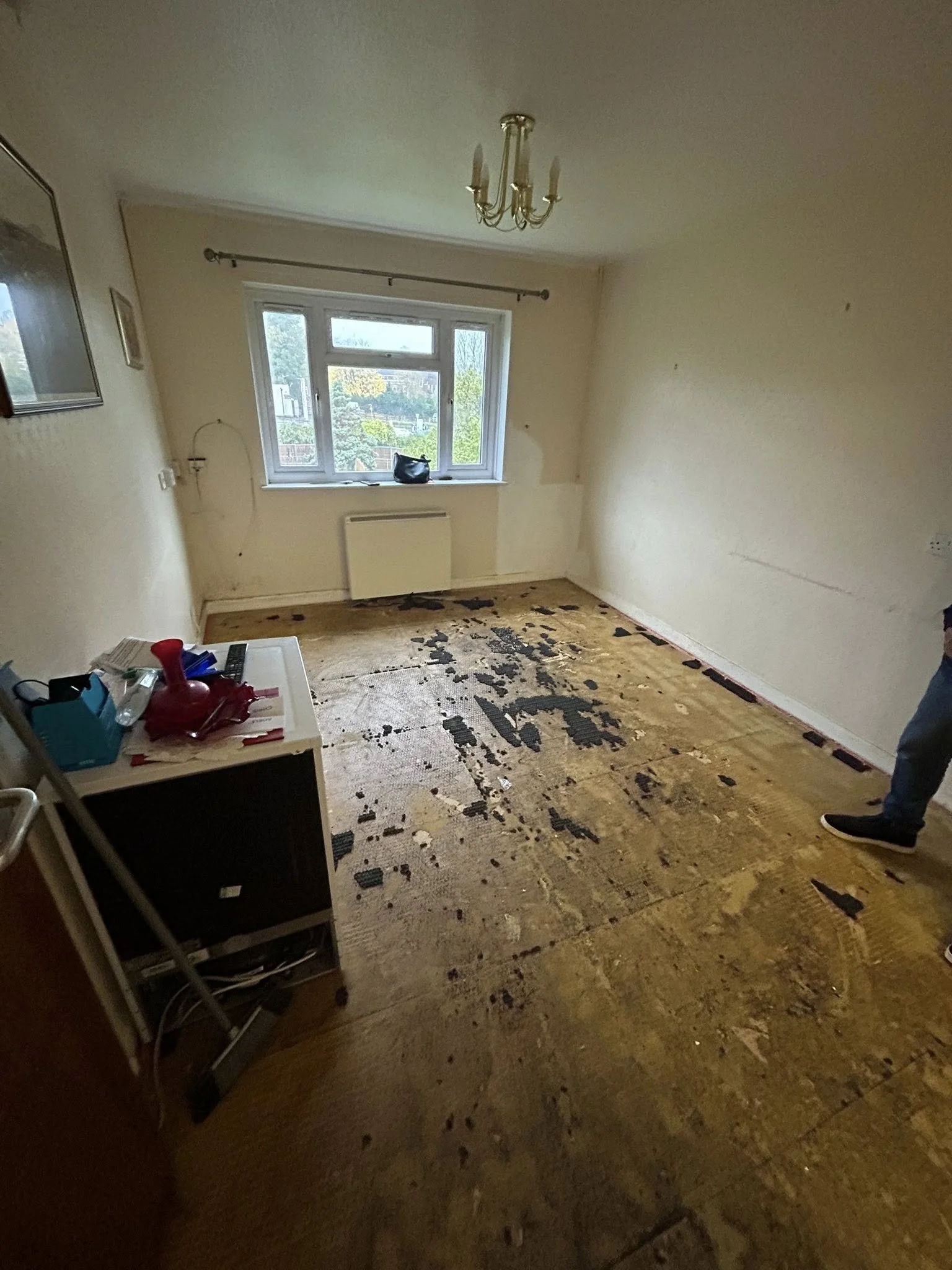 Empty room with a damaged, partially removed carpet, a window, and a chandelier hanging from the ceiling.