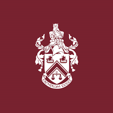 White crest with a seated eagle figure, decorative elements, and a shield with a letter 'A' on a maroon background.