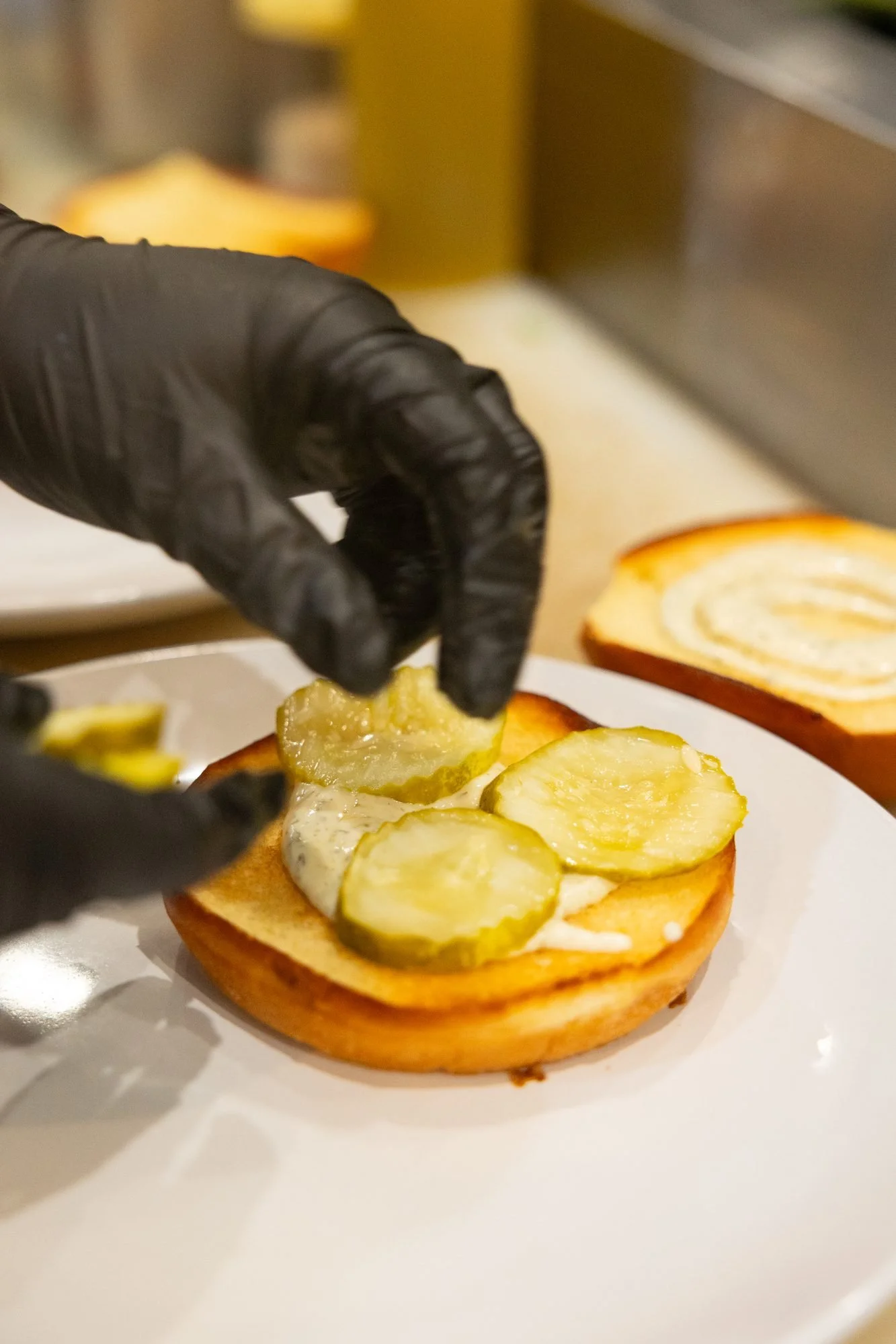 Pickle slices going onto a sandwich at the kitchen pass, brand photo for Prodigy Brewing in Logan, Utah