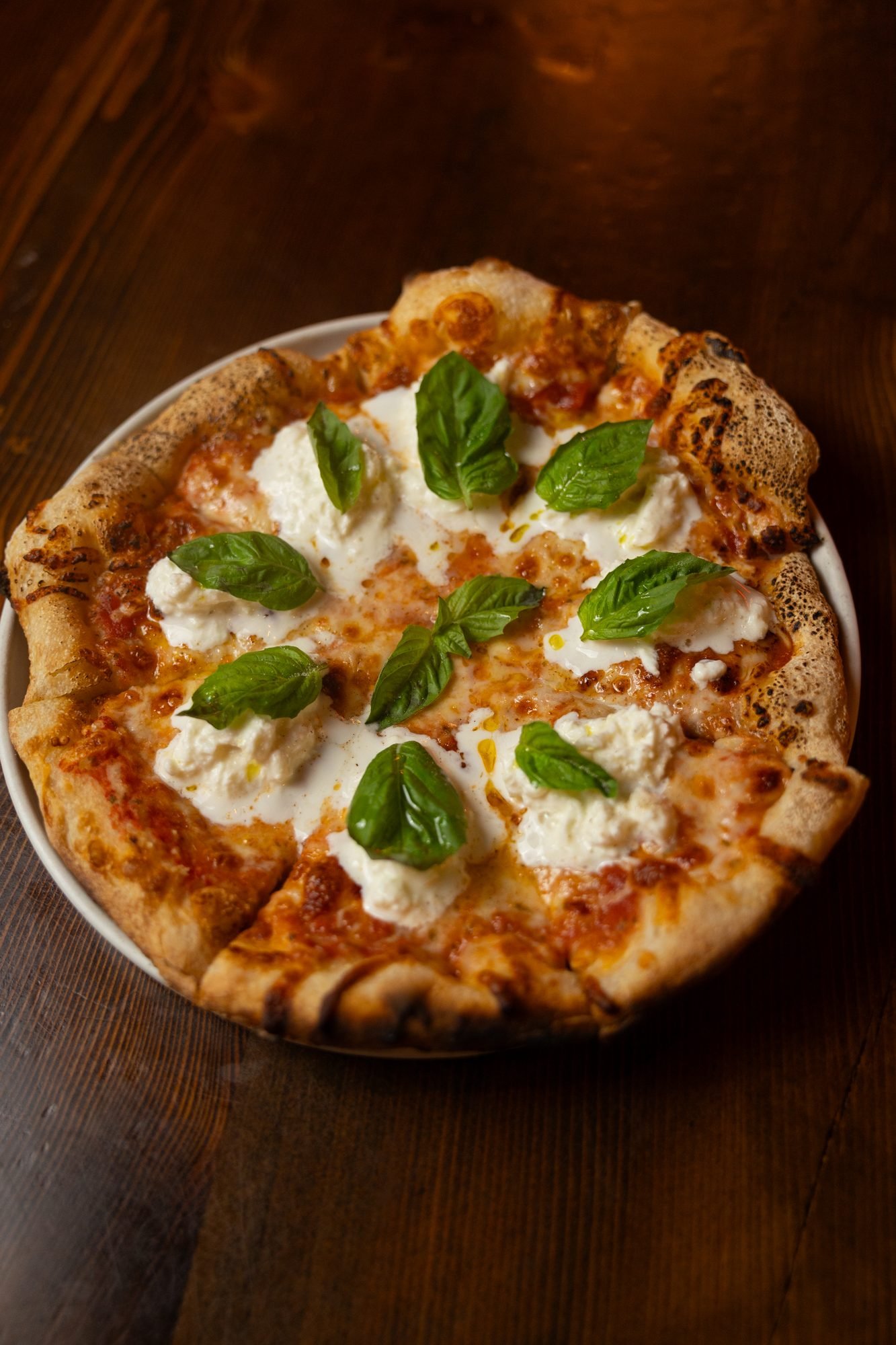 Overhead view of a small pizza topped with white cheese, red sauce, and fresh basil leaves on a dark table