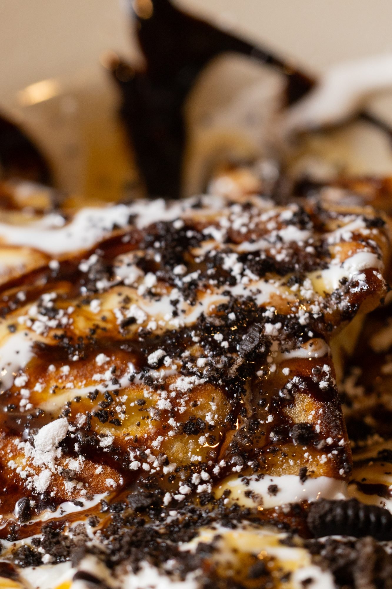 Extreme close view of whipped cream, crushed dark cookie pieces and chocolate drizzle on a folded crepe