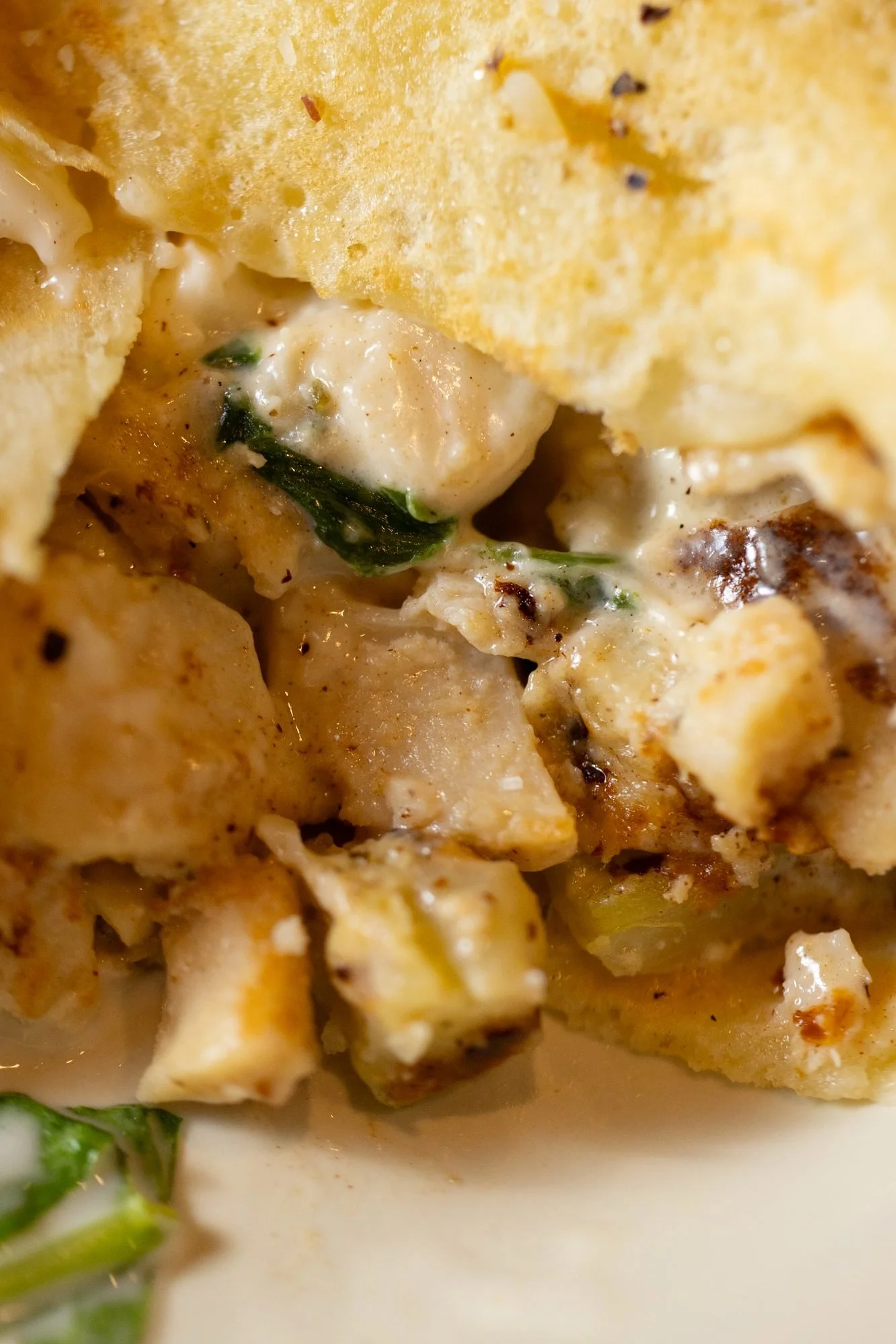 Extreme close view of chunky filling pieces with melted cheese and greens inside a crepe