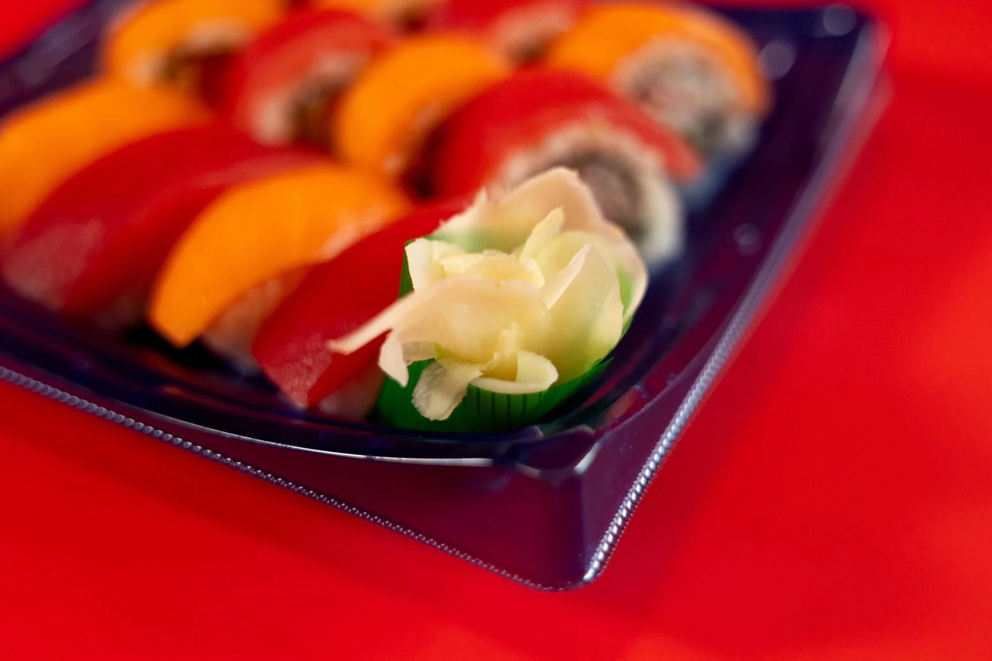Close view of tuna and salmon topped sushi rolls with pickled ginger on a dark tray against a red backdrop