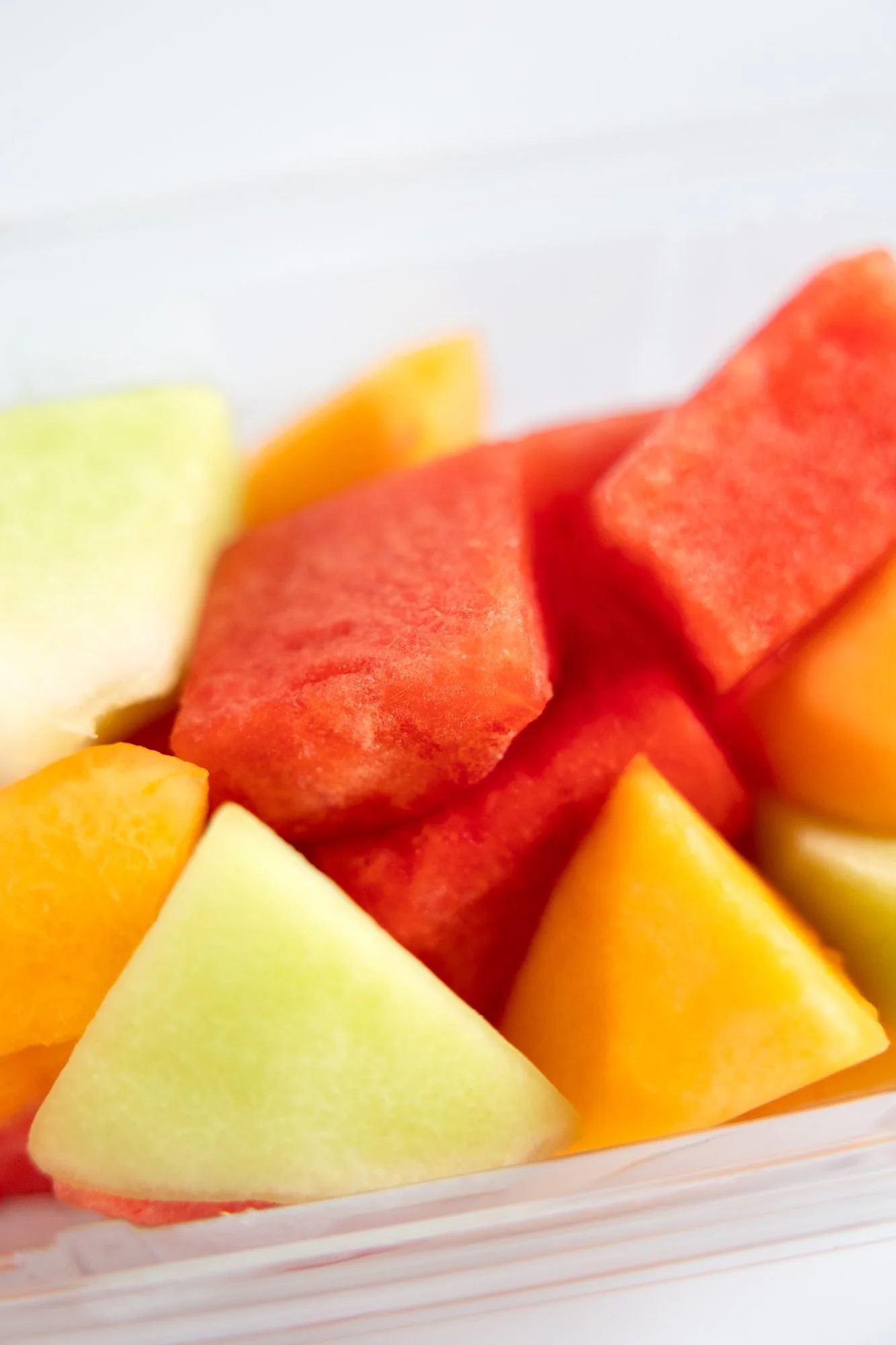 A clear container of cut watermelon, cantaloupe, and honeydew chunks on a white background