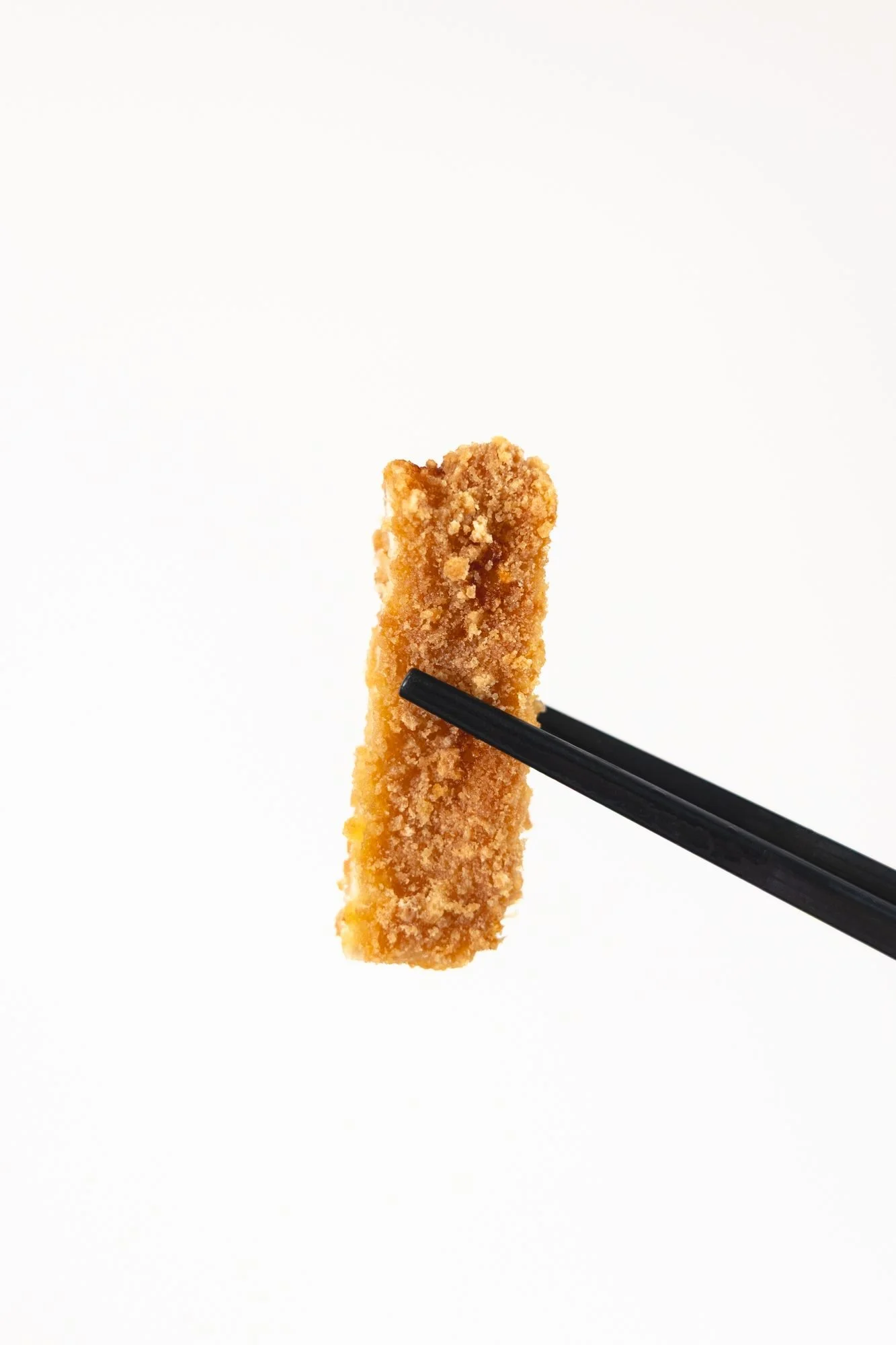 A single piece of breaded cutlet held on black chopsticks against a plain white background
