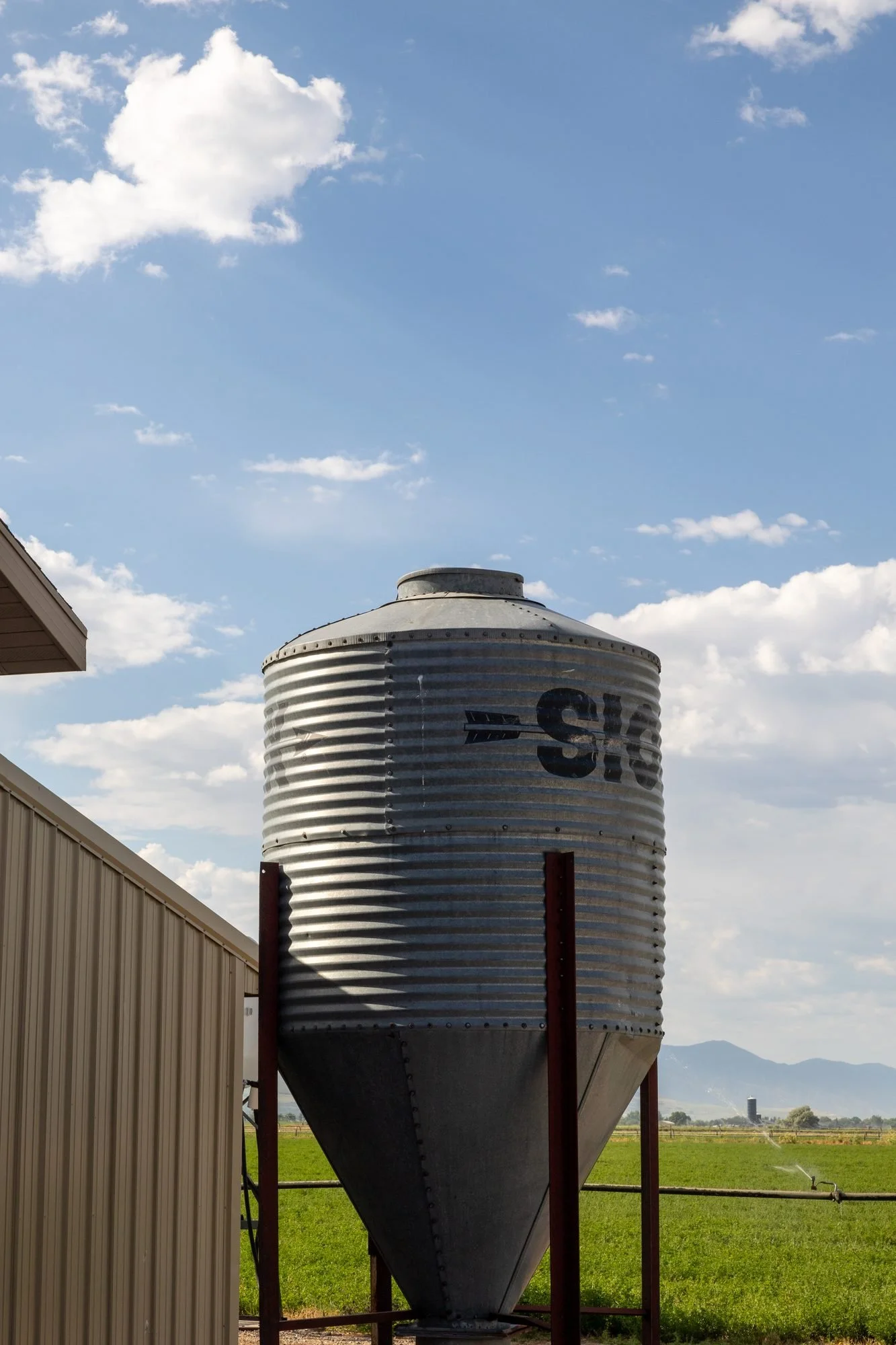 A tall metal grain silo stands against a bright blue sky with white clouds