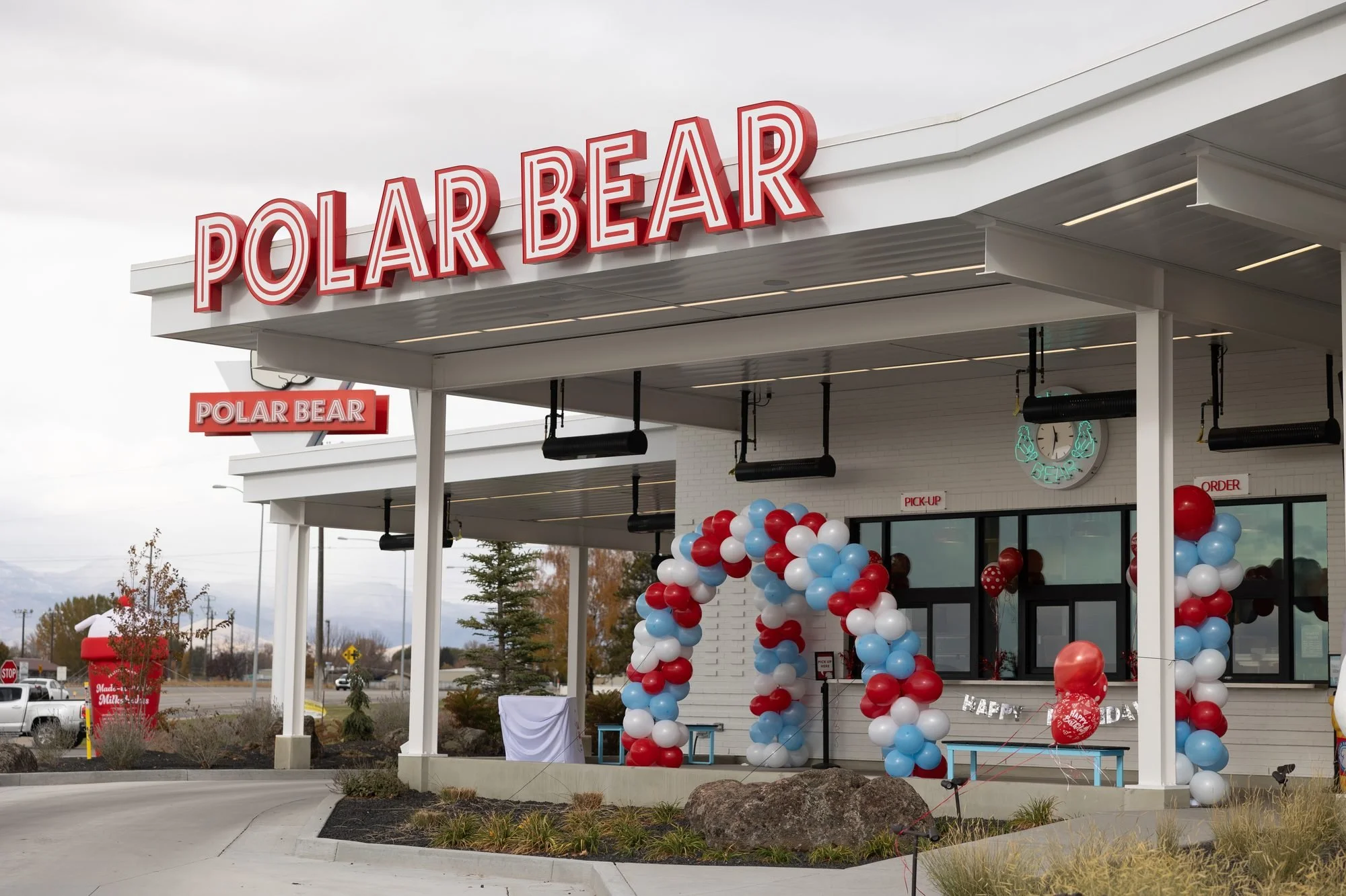 Polar Bear drive-in exterior under a gray sky with a red, white and blue balloon arch at the entrance