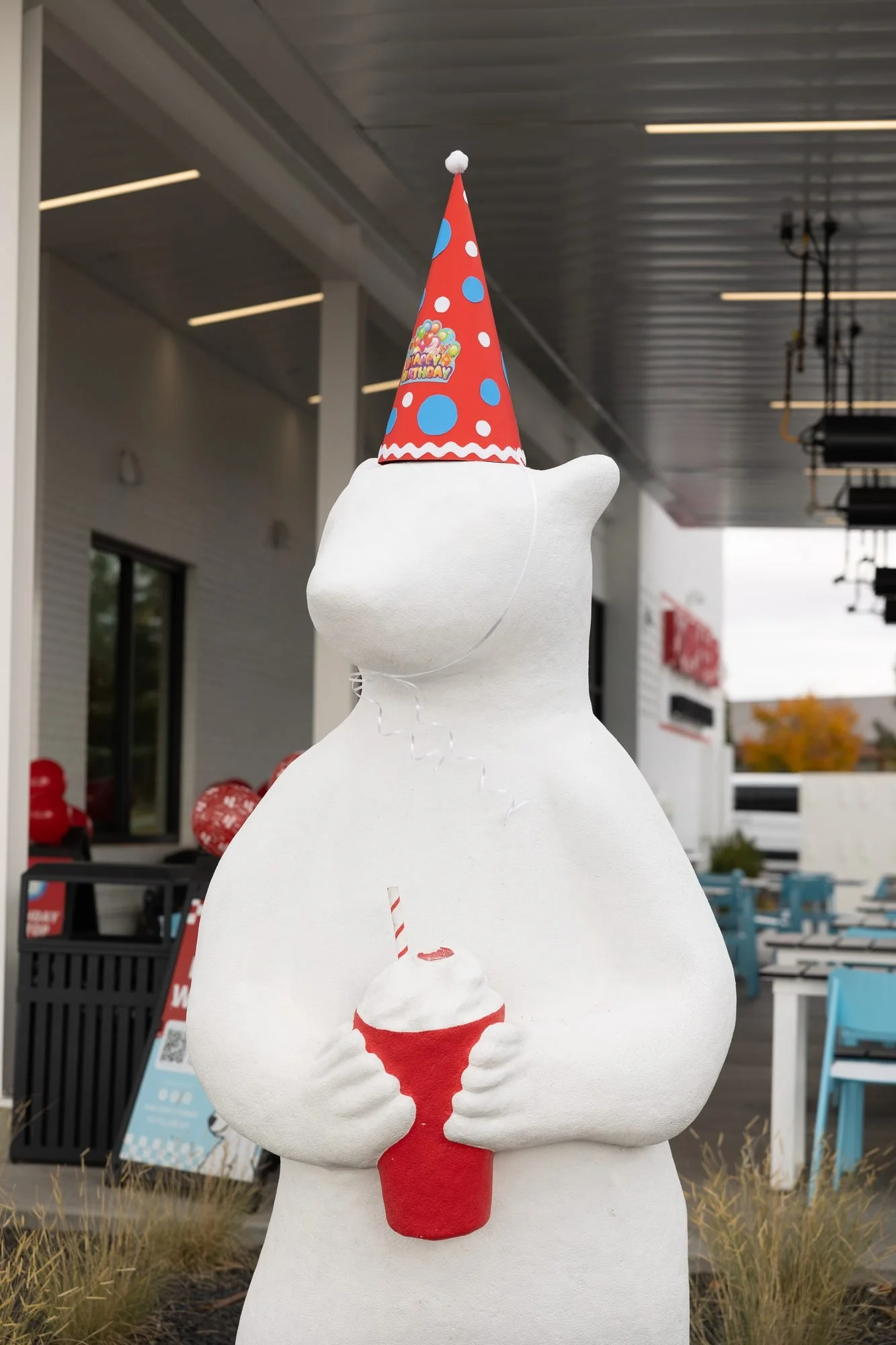 White polar bear statue wearing a red party hat and holding a red cup outside the drive-in