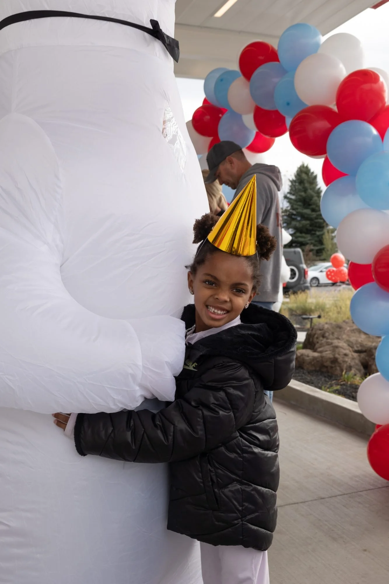 Inflatable polar bear mascot hugging a small child in a party hat beside a balloon arch