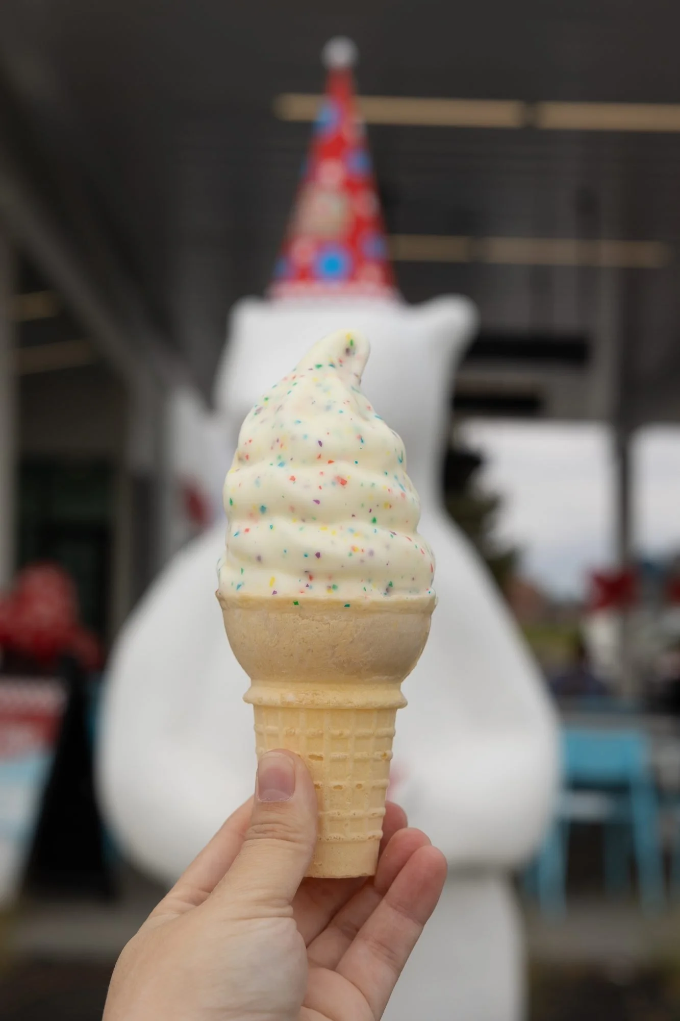 Hand holding a sprinkle dipped soft serve cone with the party hat polar bear statue blurred behind