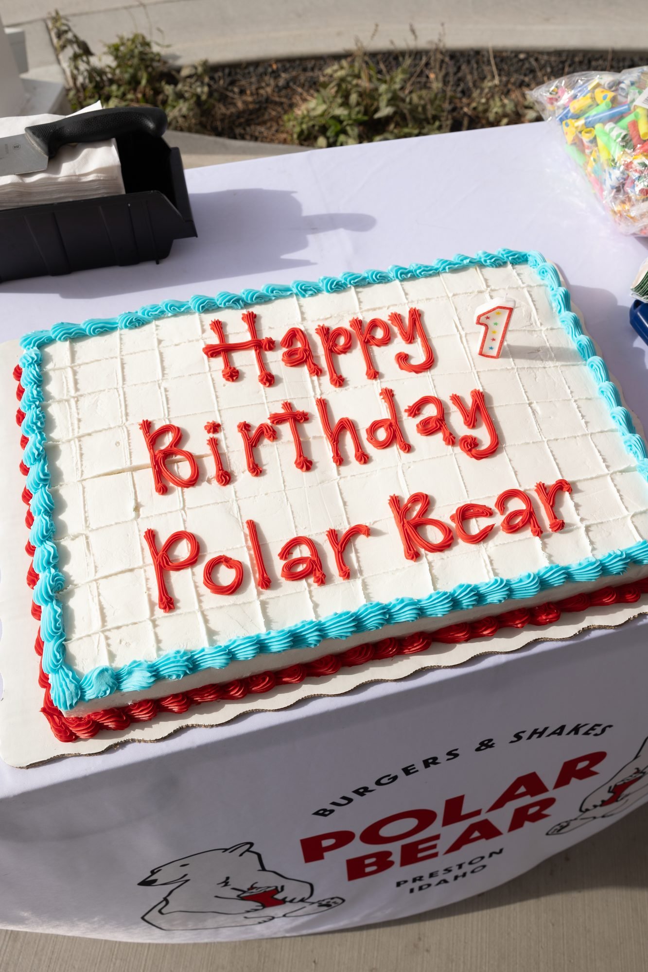 White sheet cake with Happy Birthday Polar Bear written in red icing on a branded tablecloth