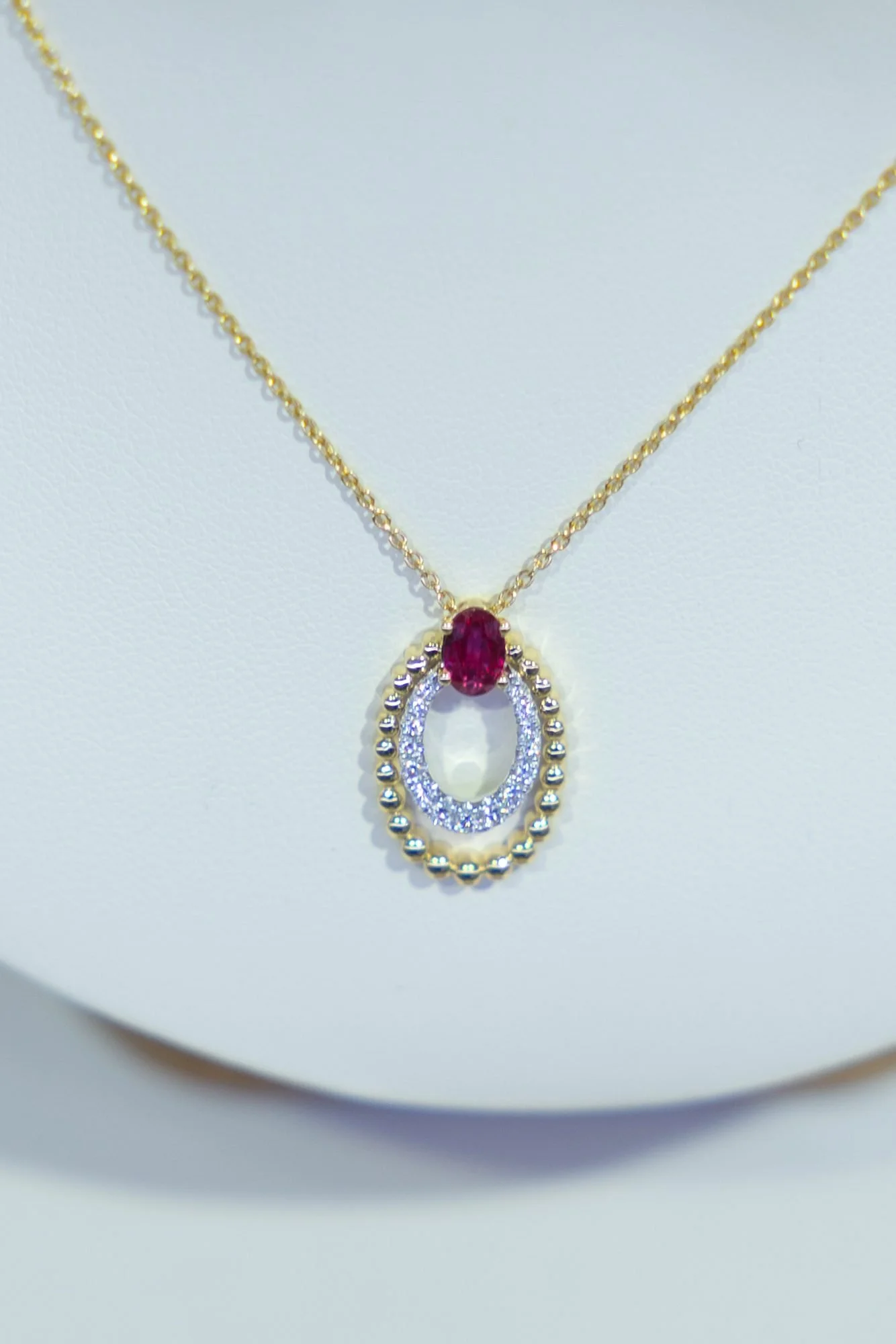 Gold necklace with an oval ruby pendant and diamond halo, product photo for Farr's Jewelry in Logan