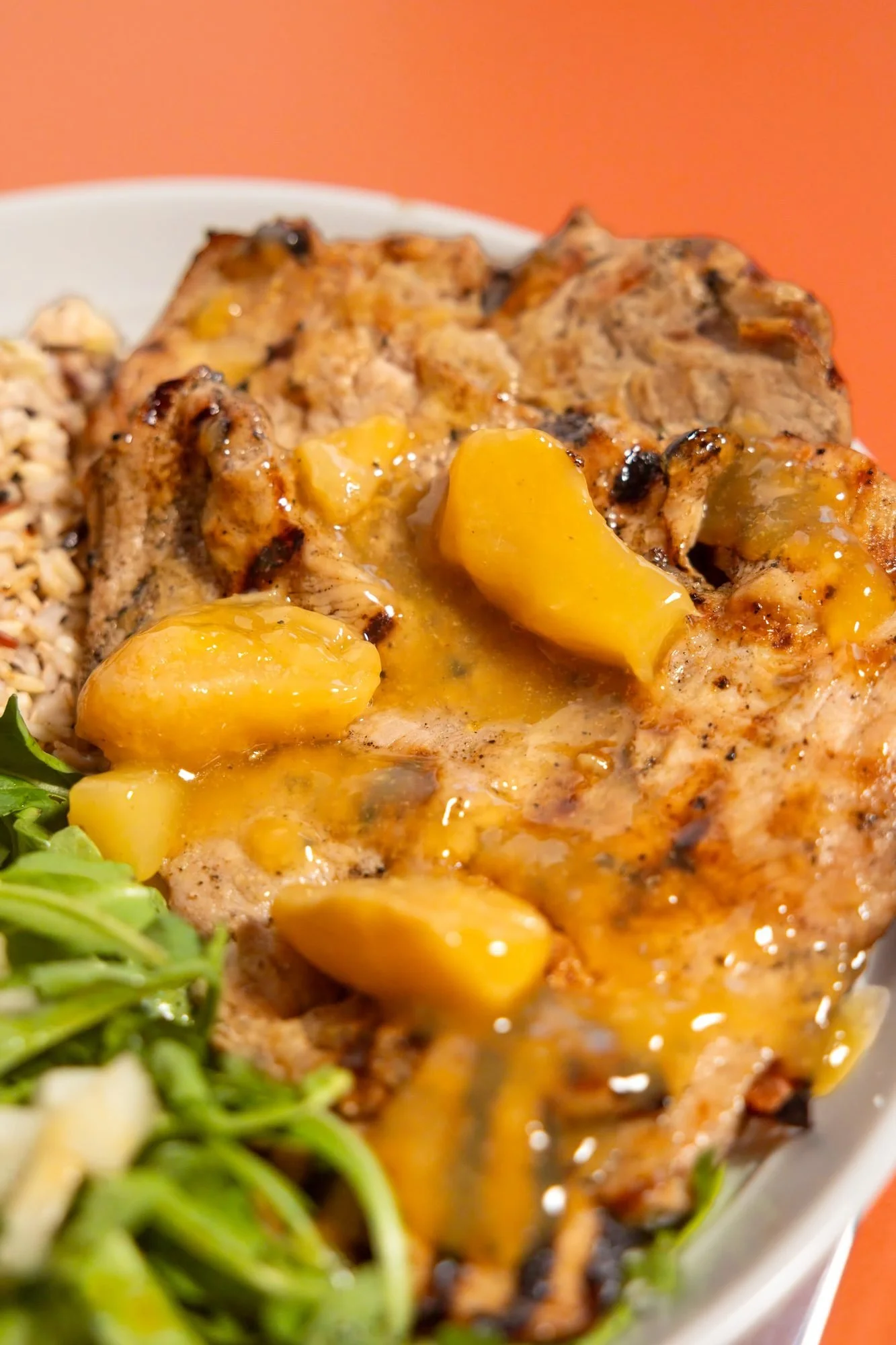 Grilled chicken with glazed peaches on an orange backdrop, meal photo for Citrus Pear in Logan