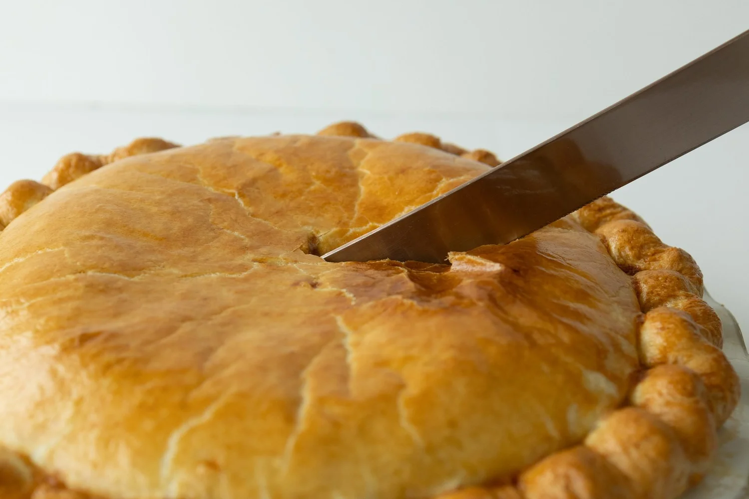 Knife cutting into a golden crimped pie, pie season photo for Crust Club