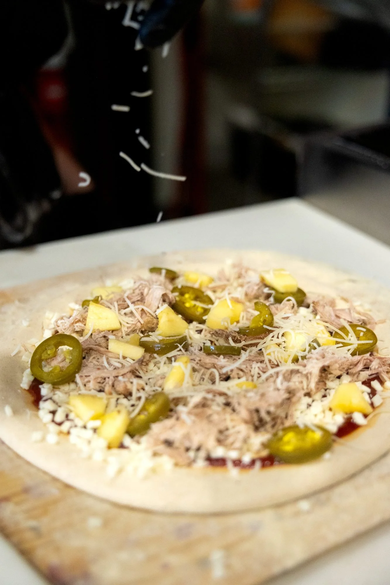 A raw pizza topped with pulled pork, jalapeno slices, pineapple and shredded cheese, ready for the oven