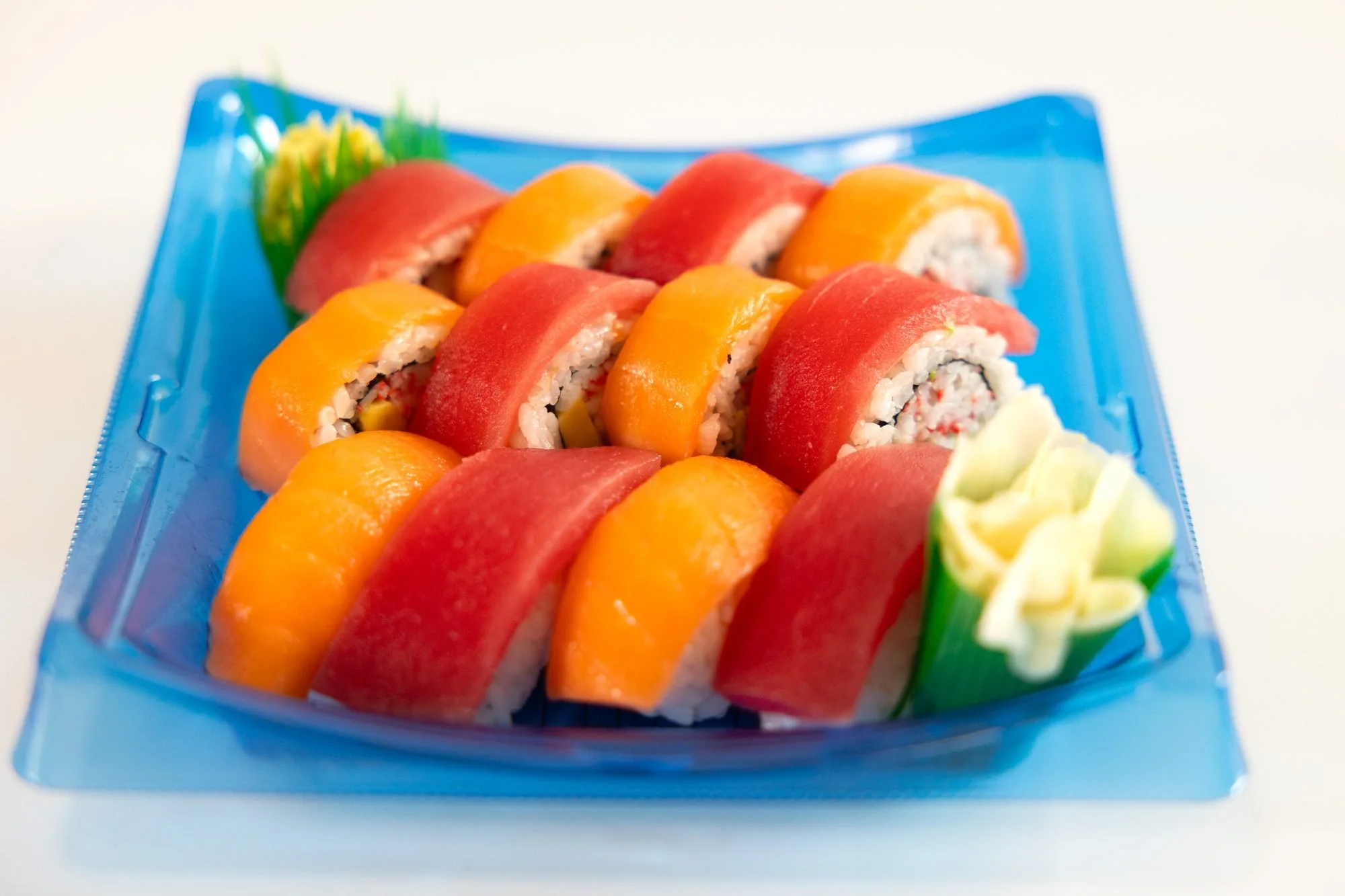 A blue tray of sushi rolls topped with tuna and salmon, with pickled ginger and wasabi
