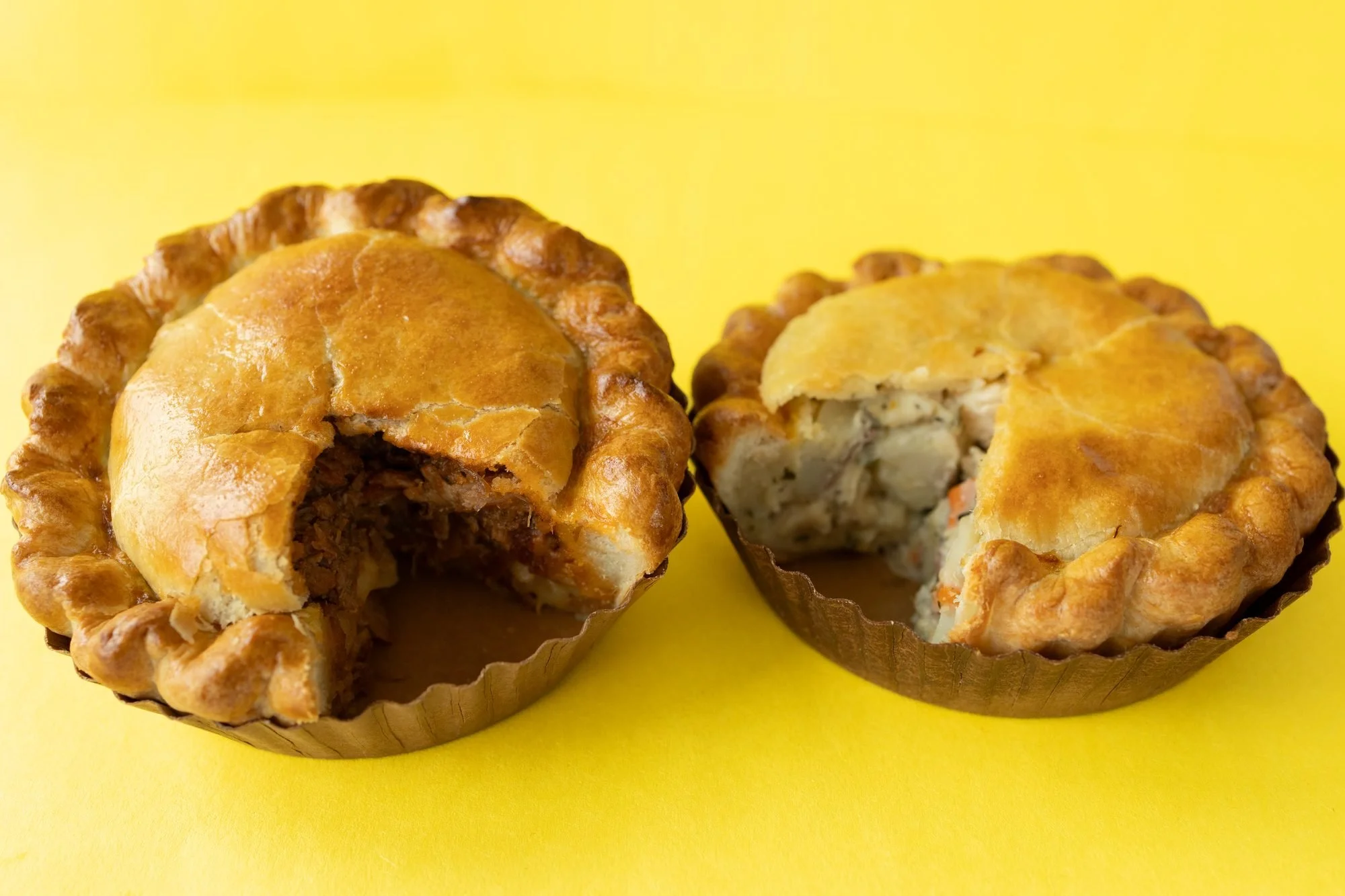 Two golden hand pies on a yellow background, one cut open to show the filling