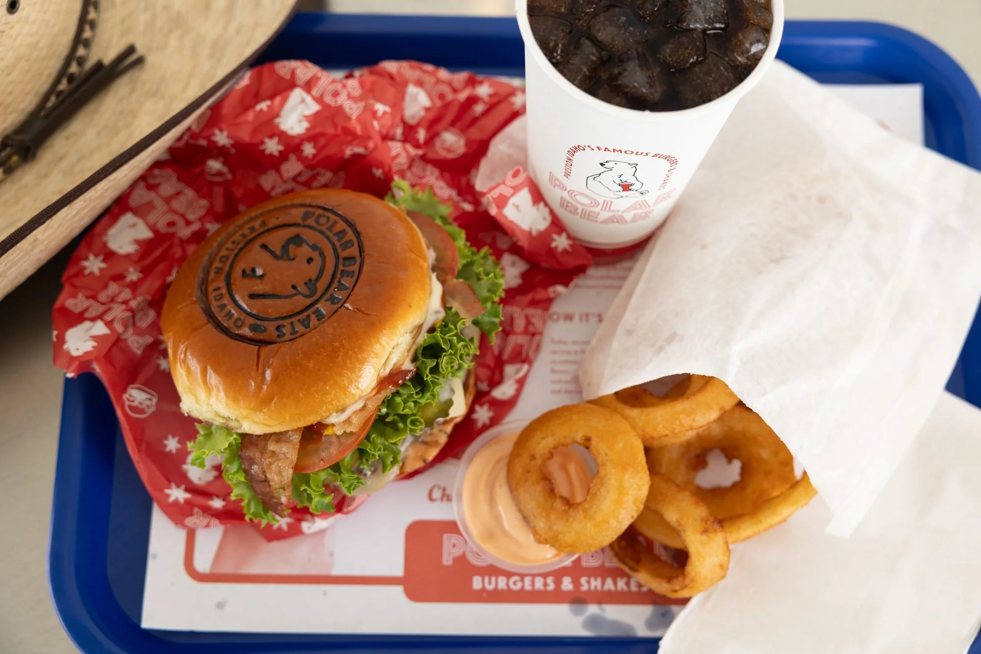 A Polar Bear tray with a cheeseburger, onion rings and a drink on red patterned paper