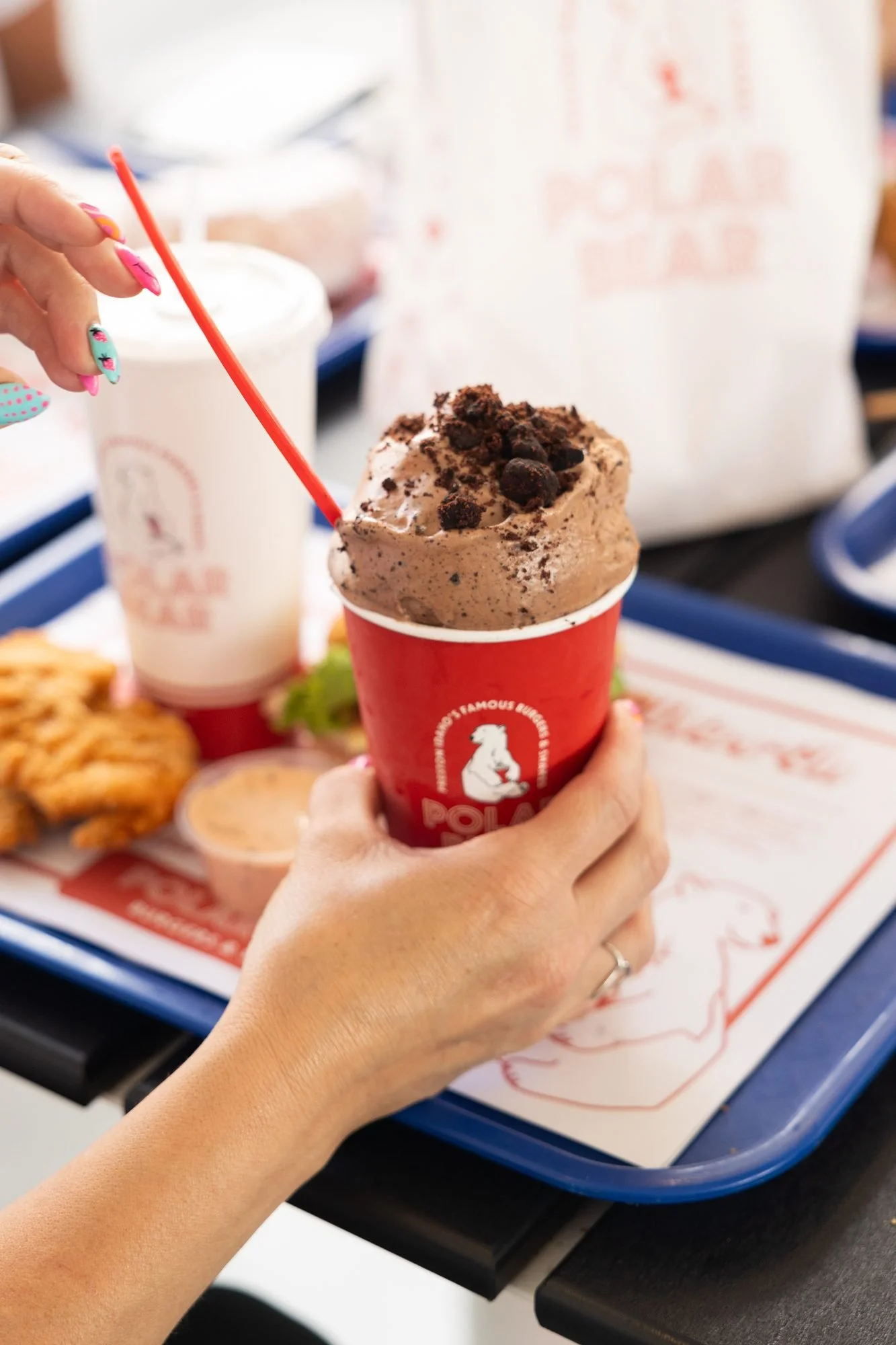 A hand holds a chocolate cookie shake in a red Polar Bear cup over a tray of food