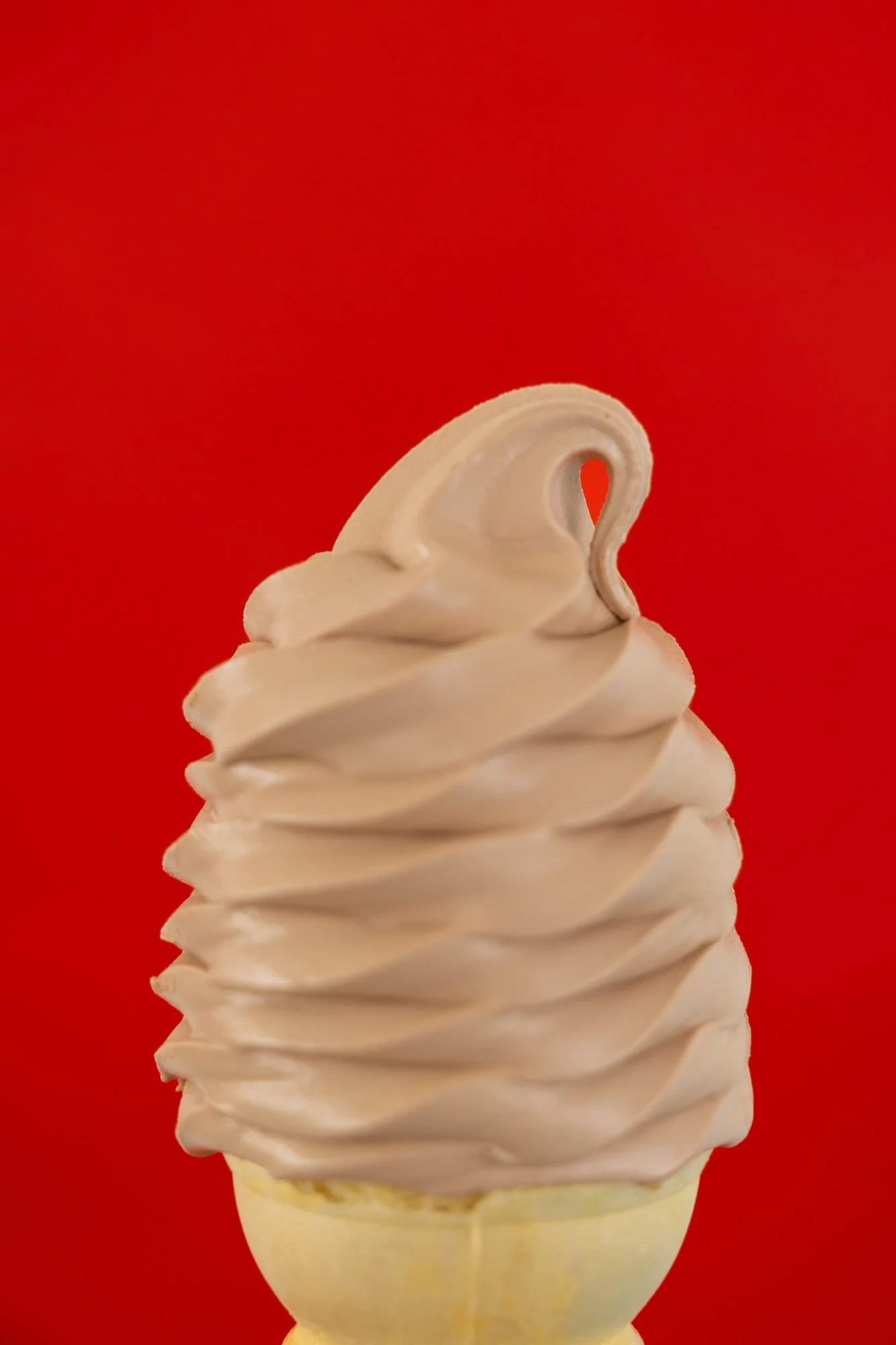 A chocolate soft-serve cone against a bright red background