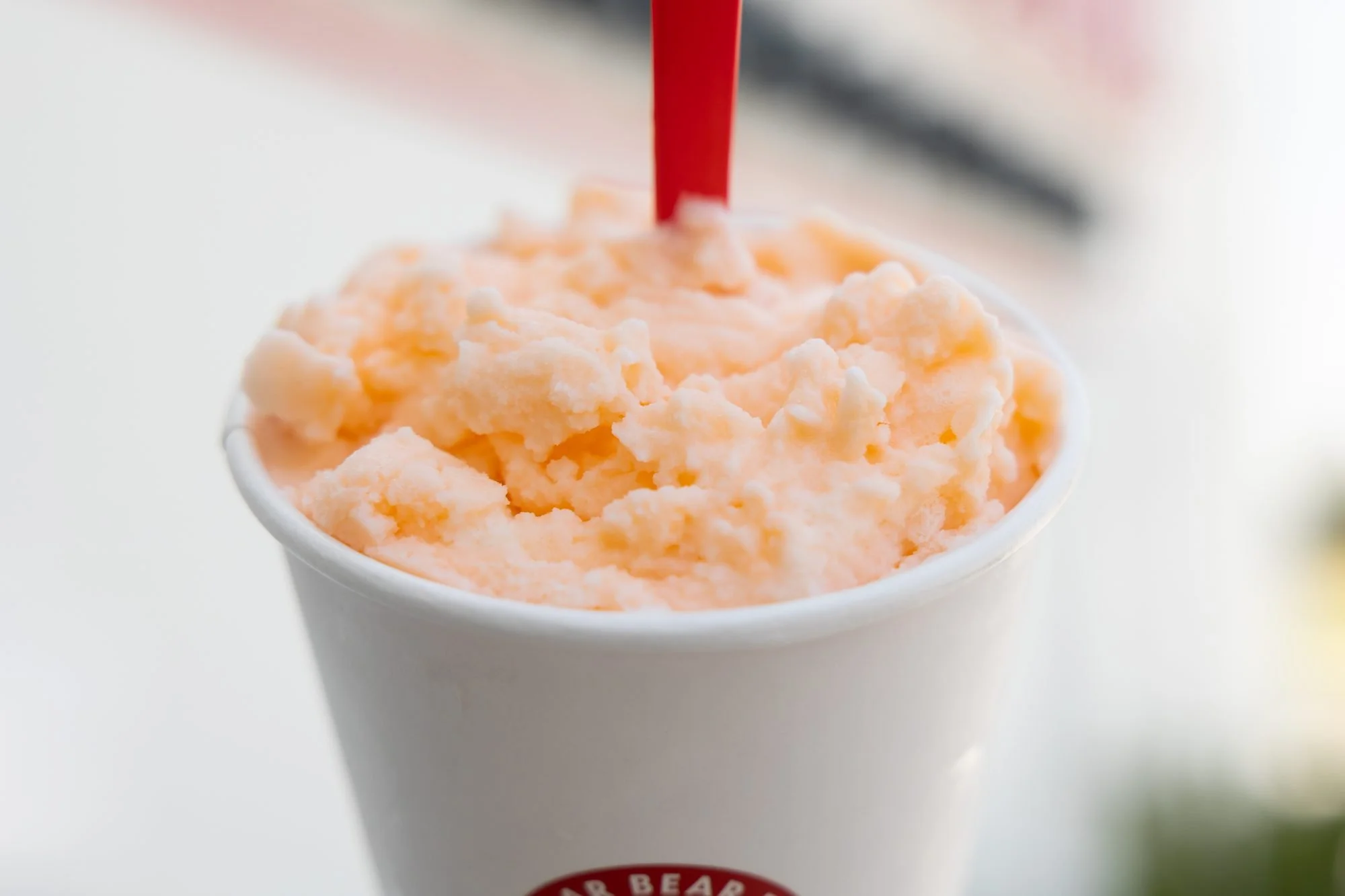 Close view of an orange sherbet shake in a Polar Bear cup with a red straw