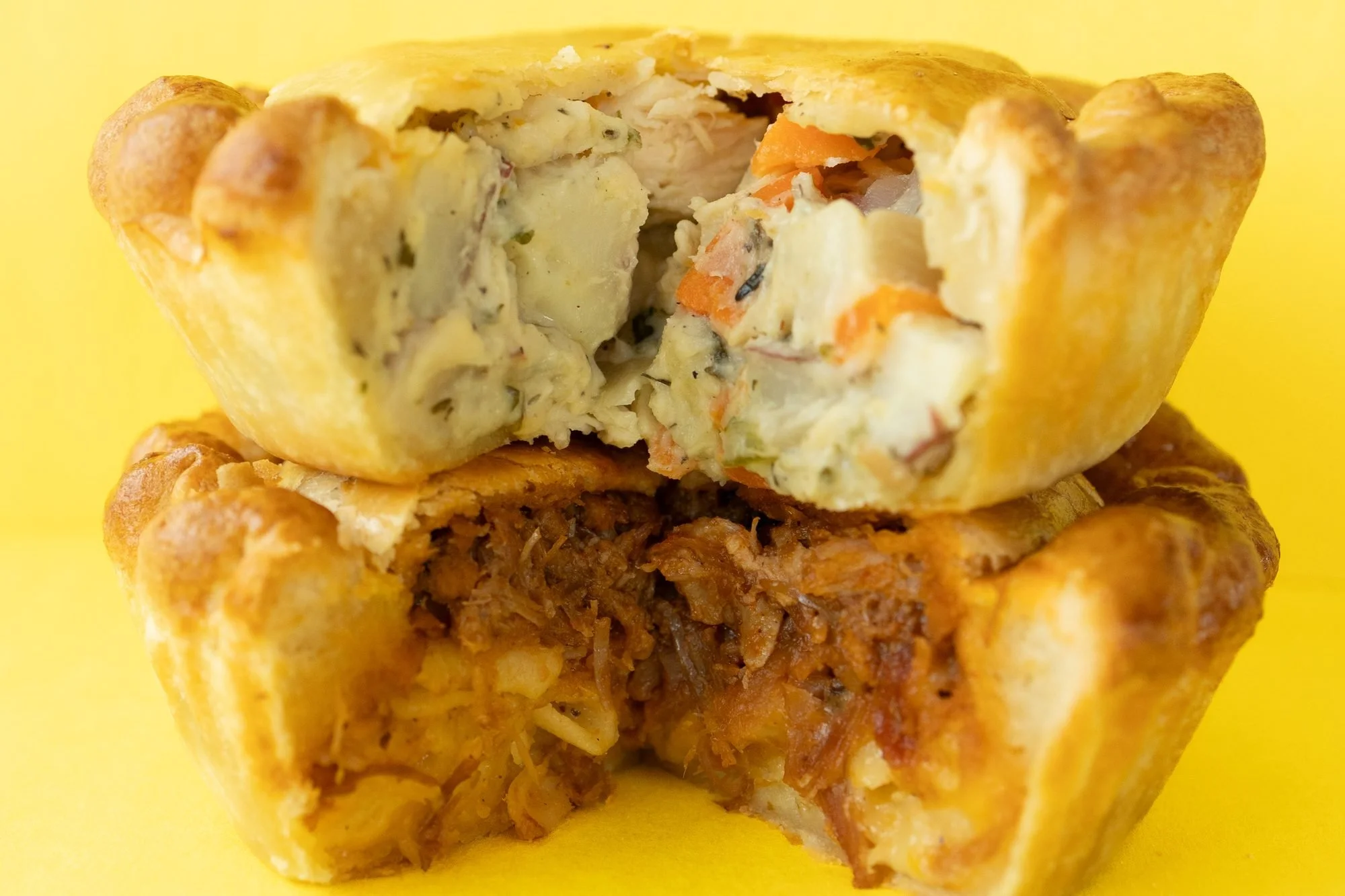 Two Crust Club hand pies stacked on a yellow background, the top one opened to show a chicken and vegetable filling
