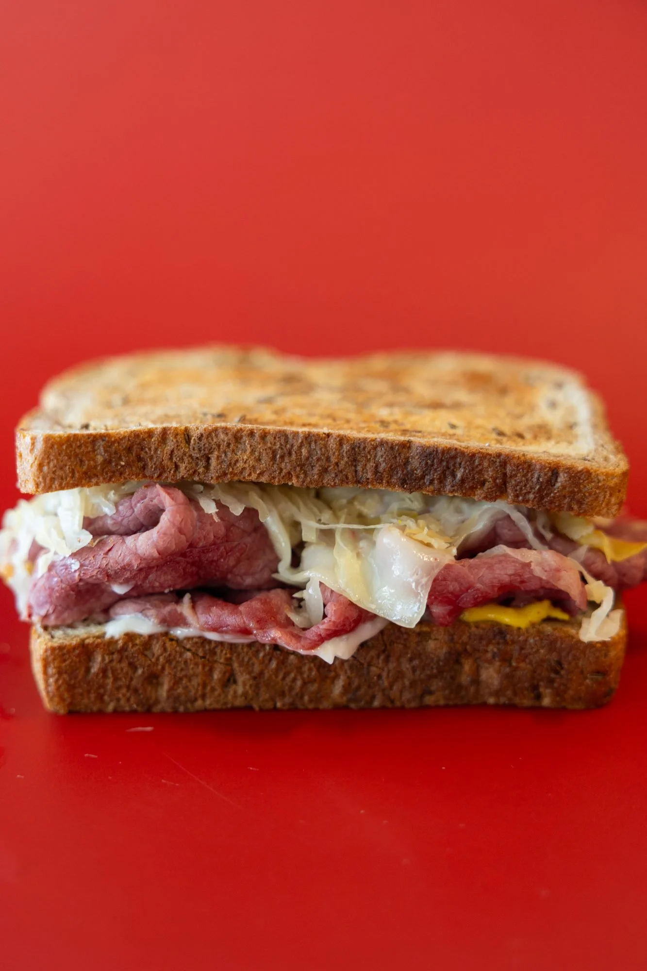 A thick sandwich of roast beef and sauerkraut on toasted rye against a red background