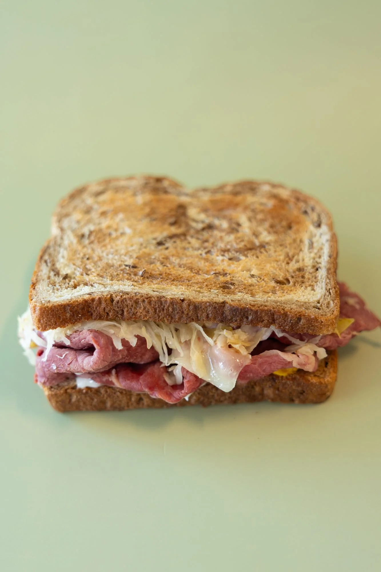 A toasted rye sandwich of roast beef and sauerkraut on a pale green background