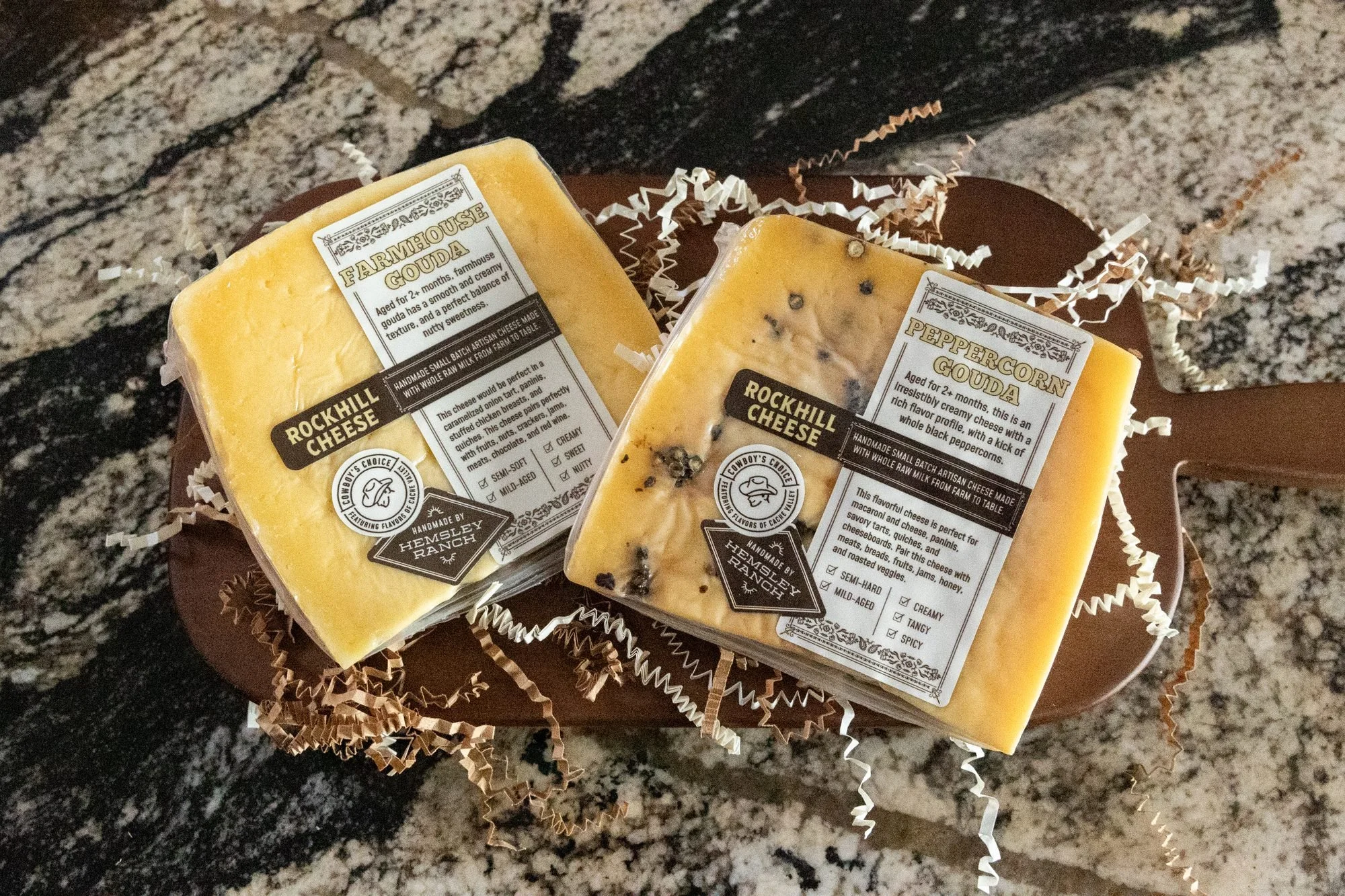 Two wrapped cheese wedges on a wooden board on a granite counter