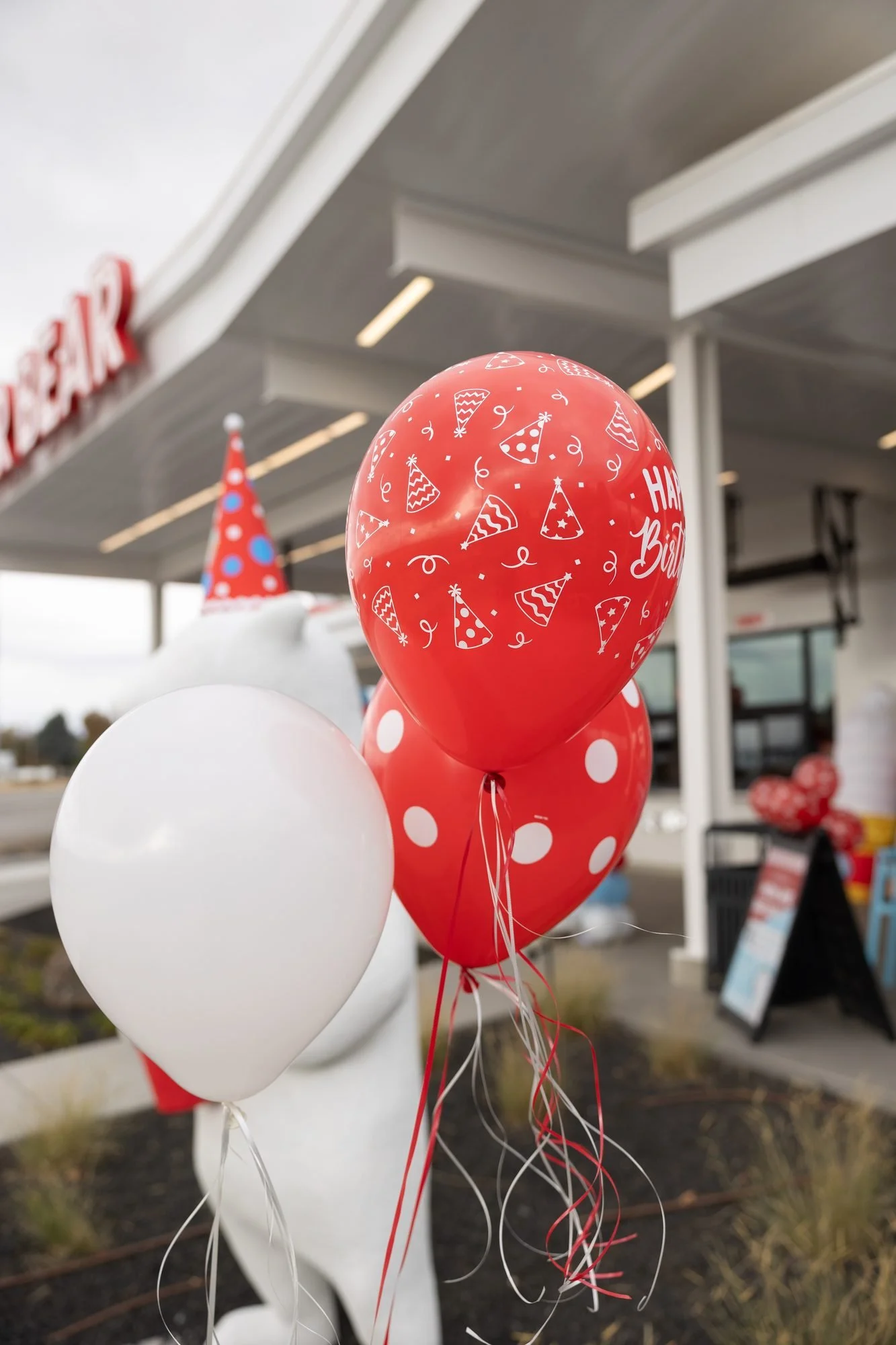 A polar bear statue in a party hat stands beside red and white birthday balloons