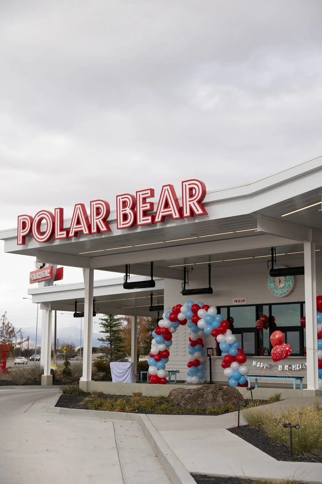 A Polar Bear drive-in with its red sign and a red, white and blue balloon arch under a cloudy sky