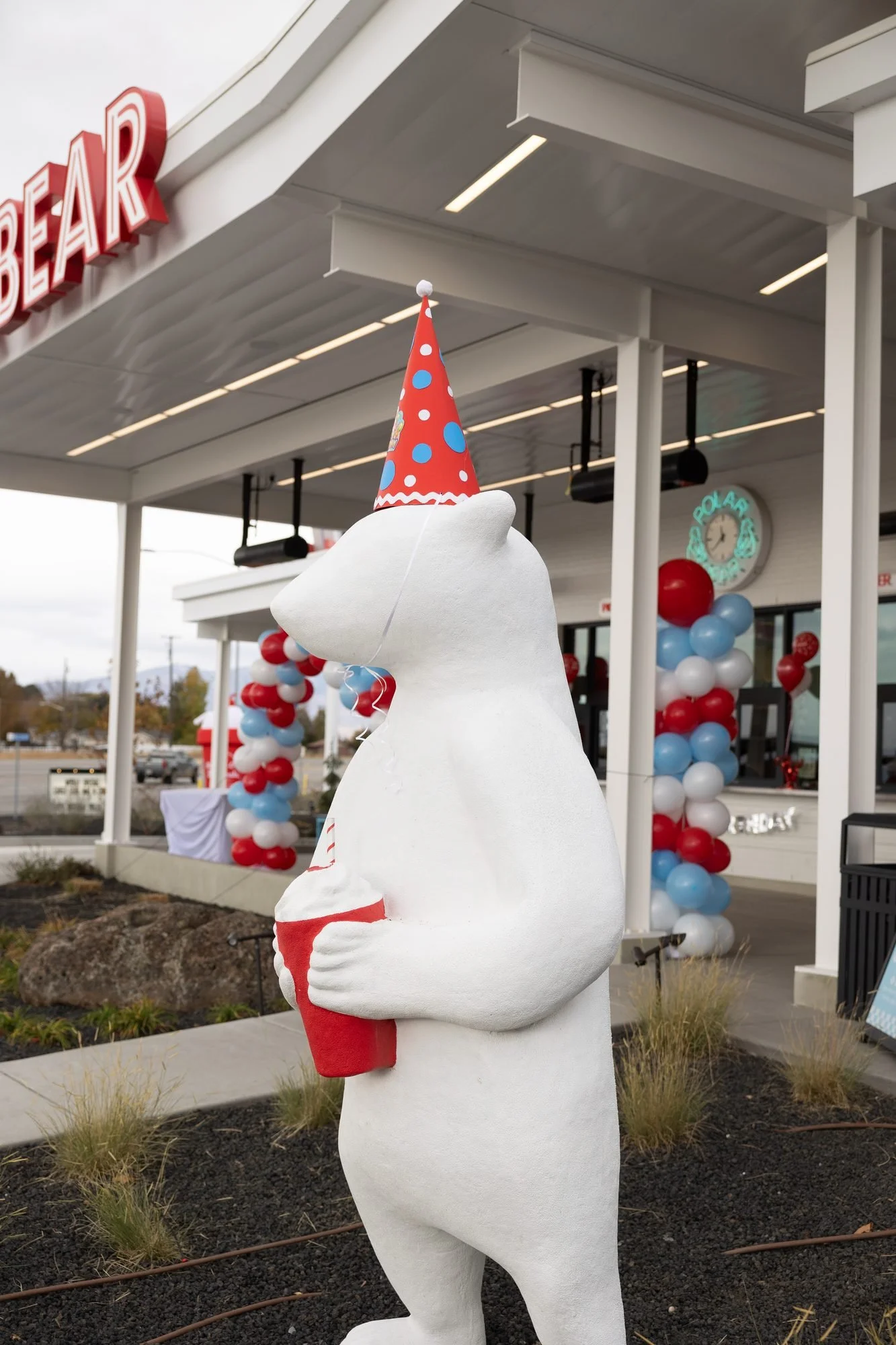 A white polar bear statue wearing a party hat outside a shop decorated with balloons