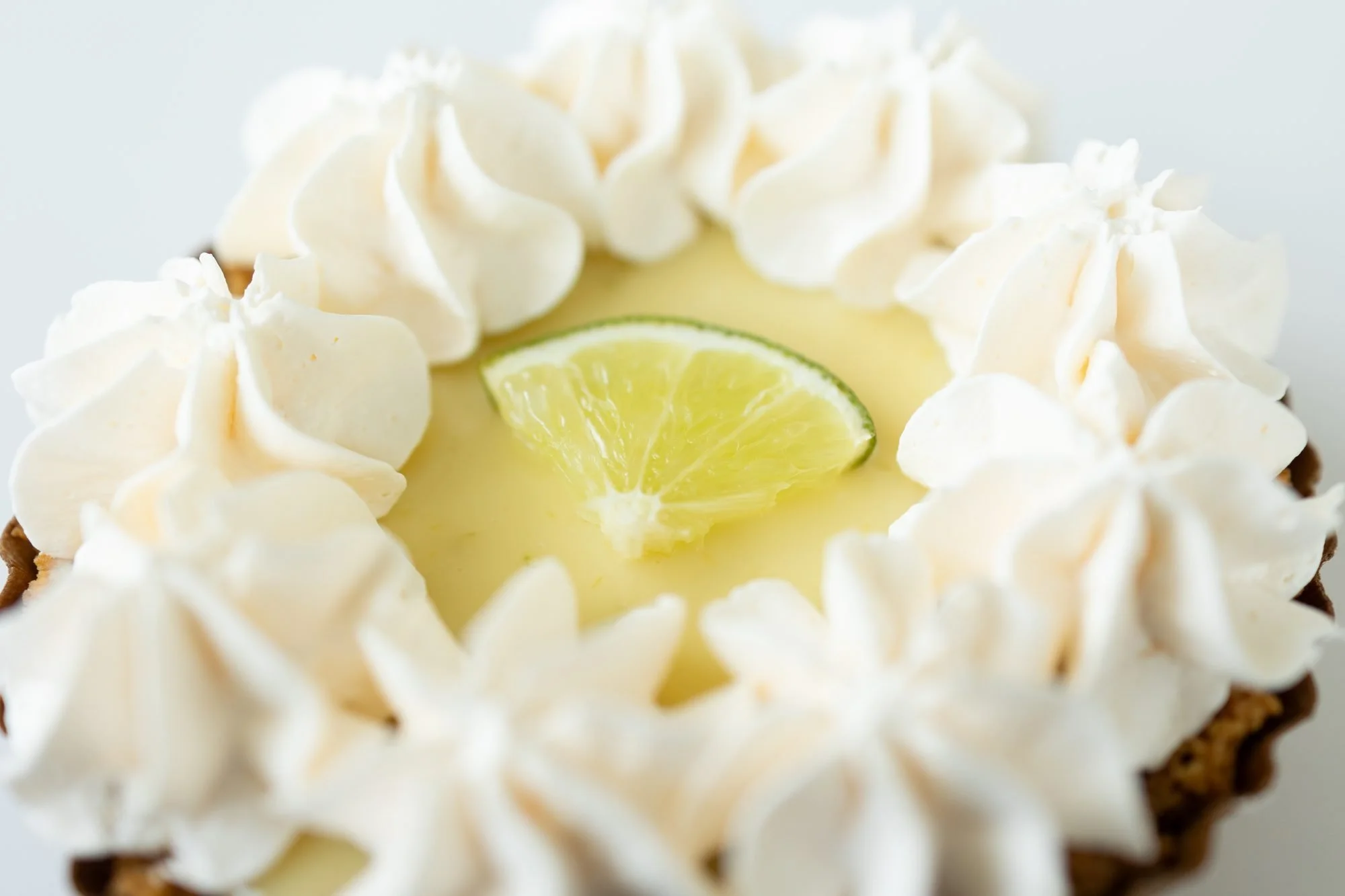 Close view of a Crust Club key lime pie with piped whipped cream and a lime slice