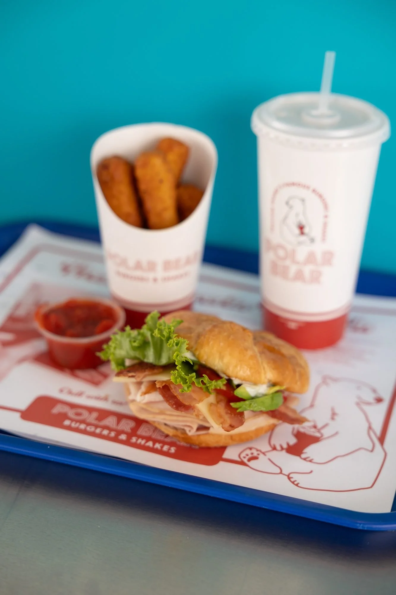 A Polar Bear tray with a club sandwich, mozzarella sticks, a drink and ketchup