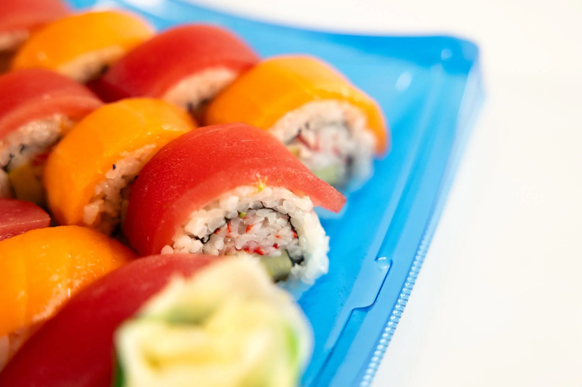 Close view of sushi rolls topped with tuna and salmon on a blue tray