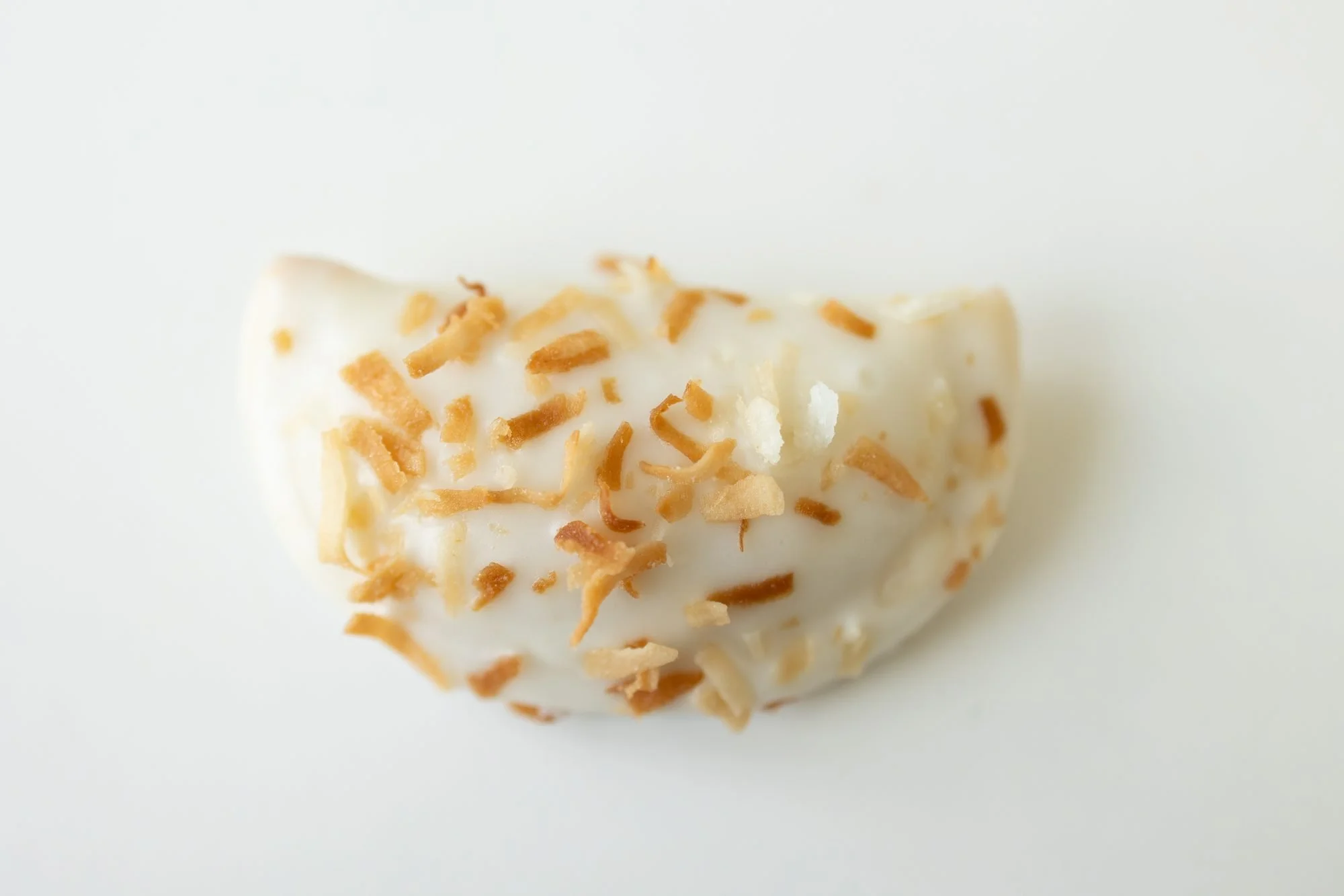 A glazed hand pie topped with toasted coconut on a white background