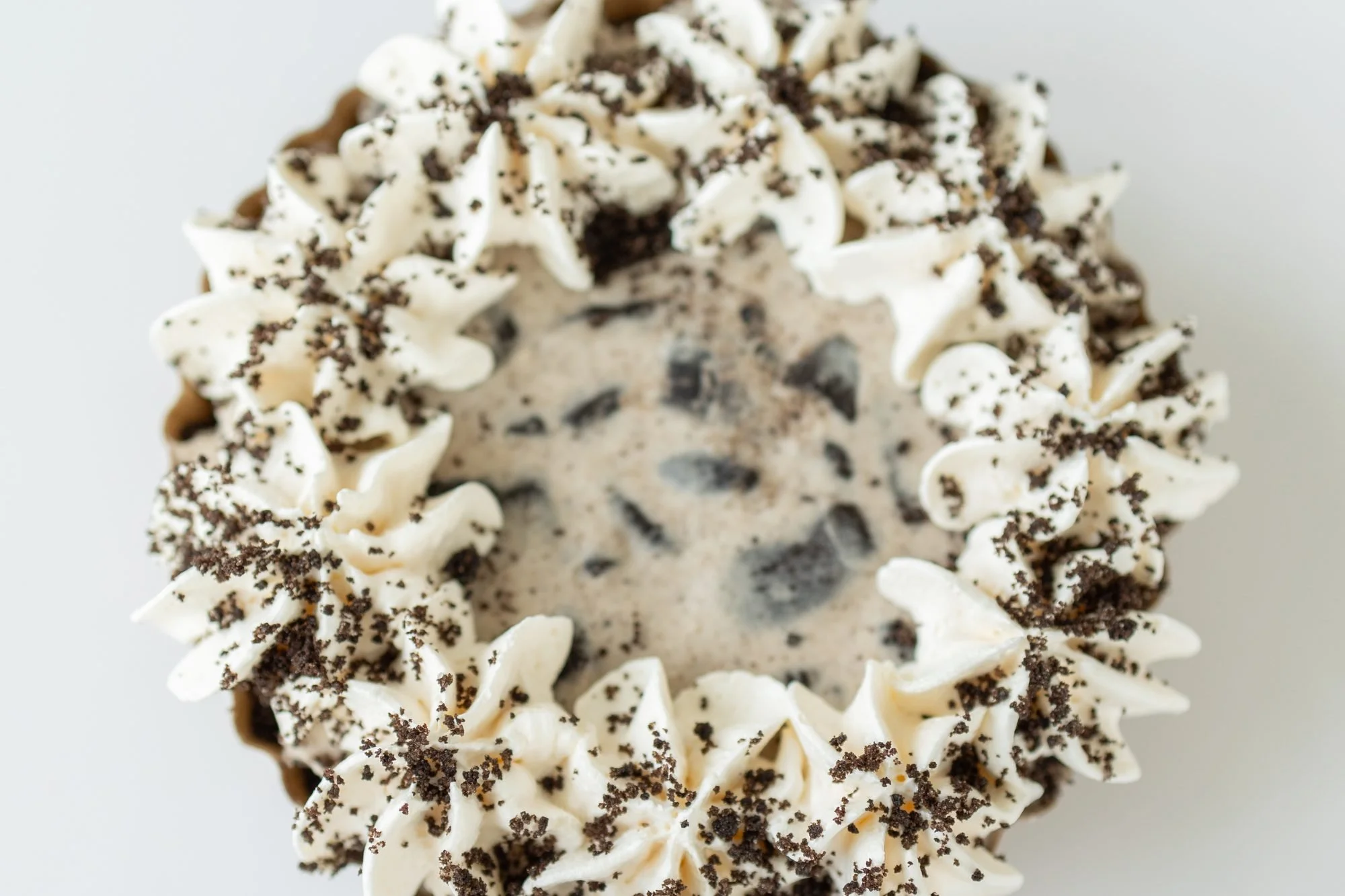 A Crust Club cookies and cream pie with piped cream and cookie crumbs on a white surface