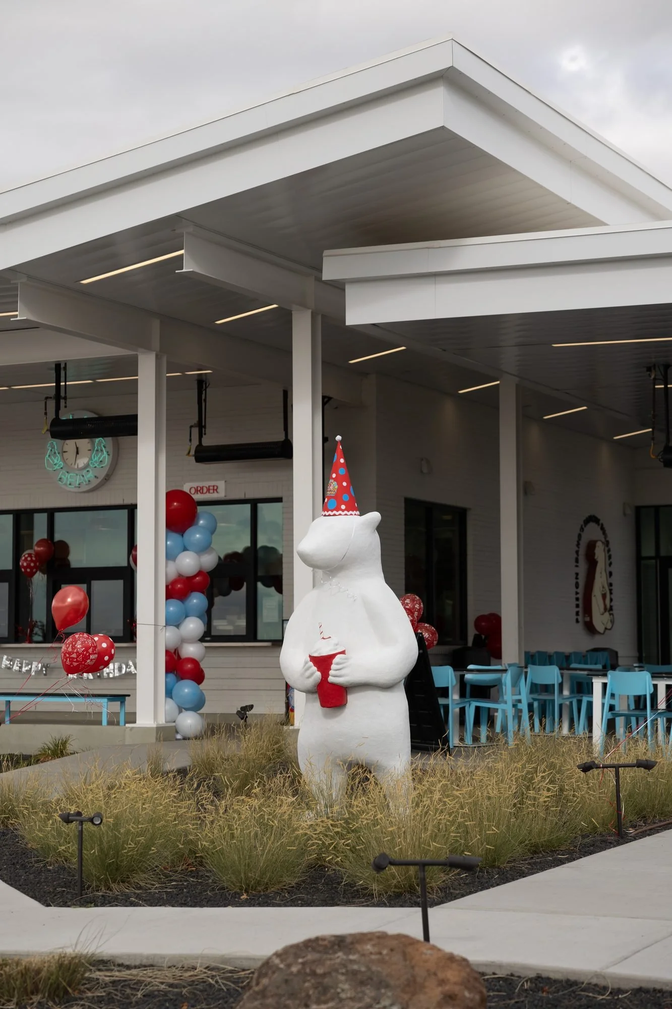 A white polar bear statue in a party hat under the canopy of a drive-in decorated with balloons