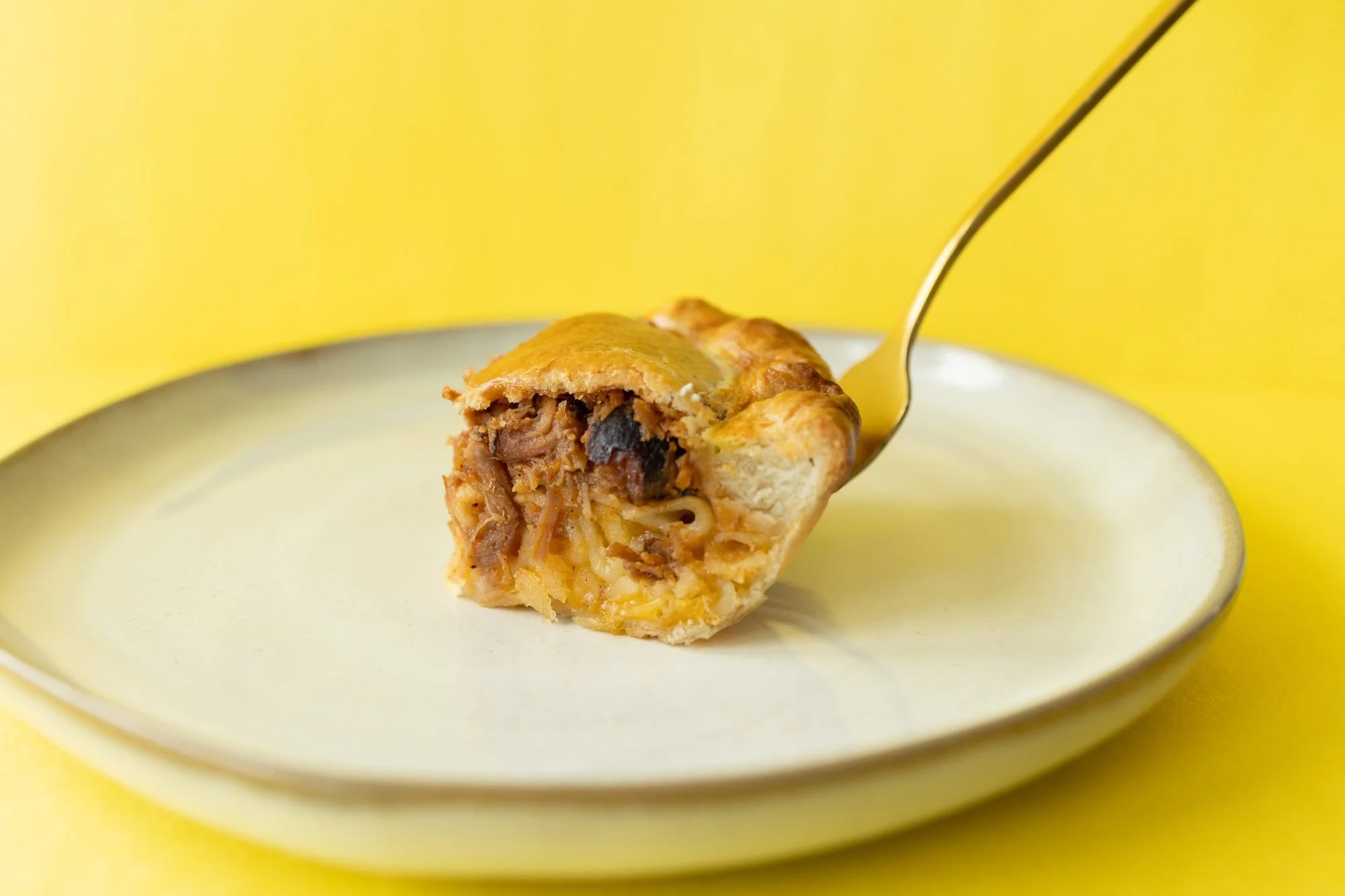 A Crust Club hand pie with a bite lifted on a gold fork, on a plate against a bright yellow background