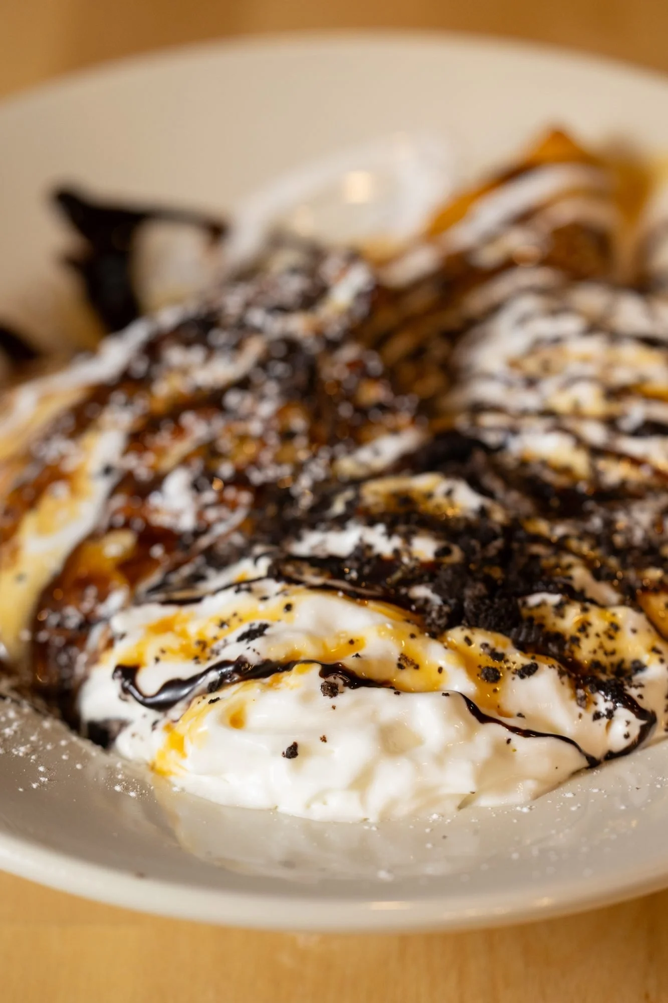 Close view of a crepe topped with whipped cream, cookie crumbs, caramel and chocolate drizzle