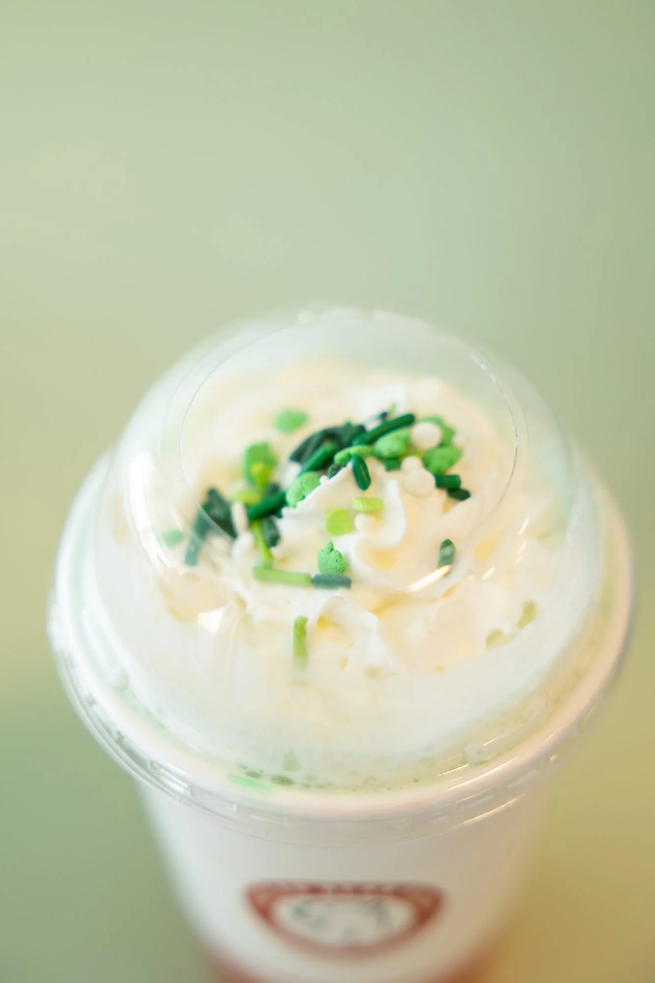 A shake topped with whipped cream and green sprinkles in a clear-lidded cup