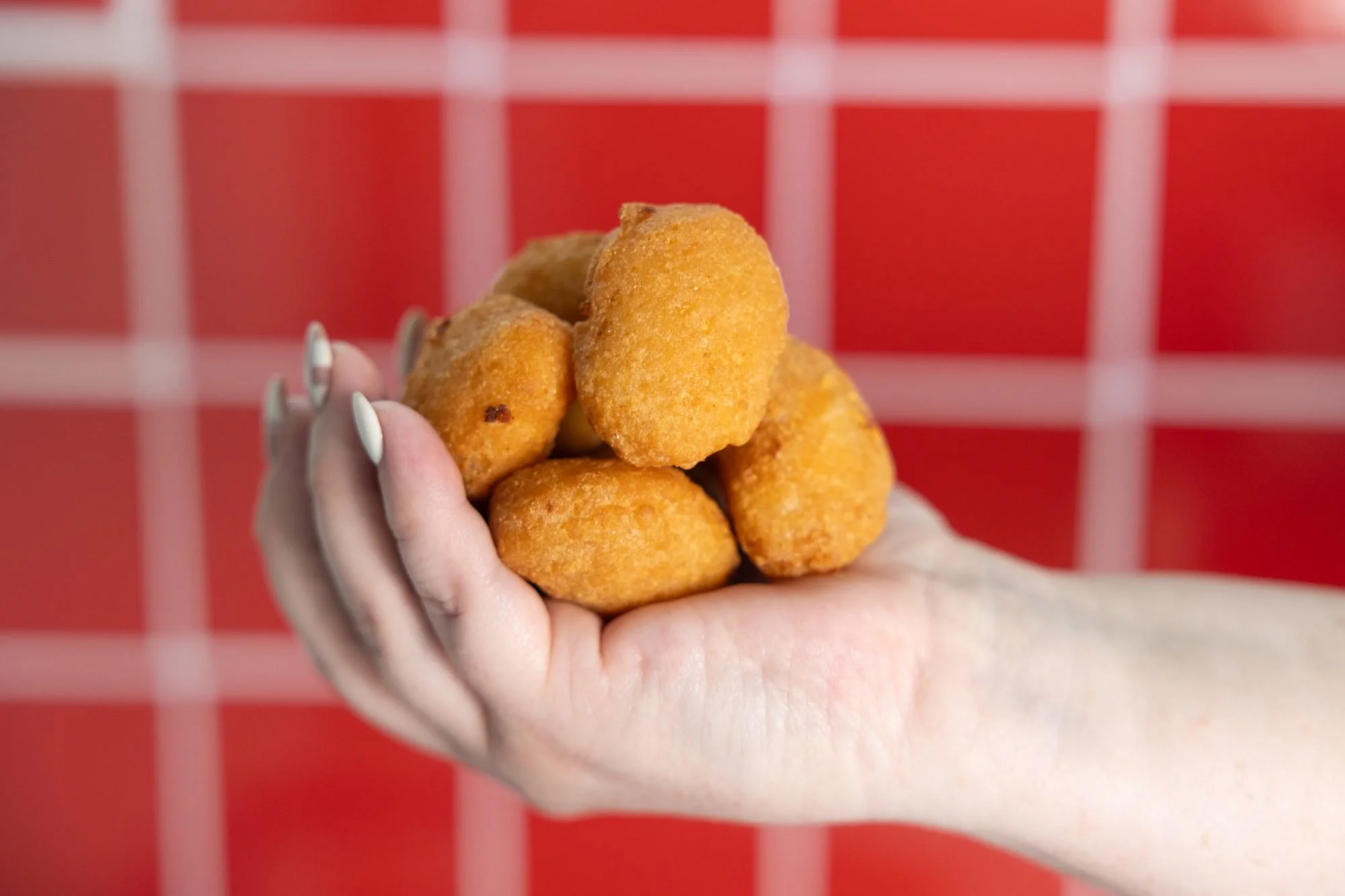 A hand holding a pile of golden fried cheese curds in front of a red tiled wall